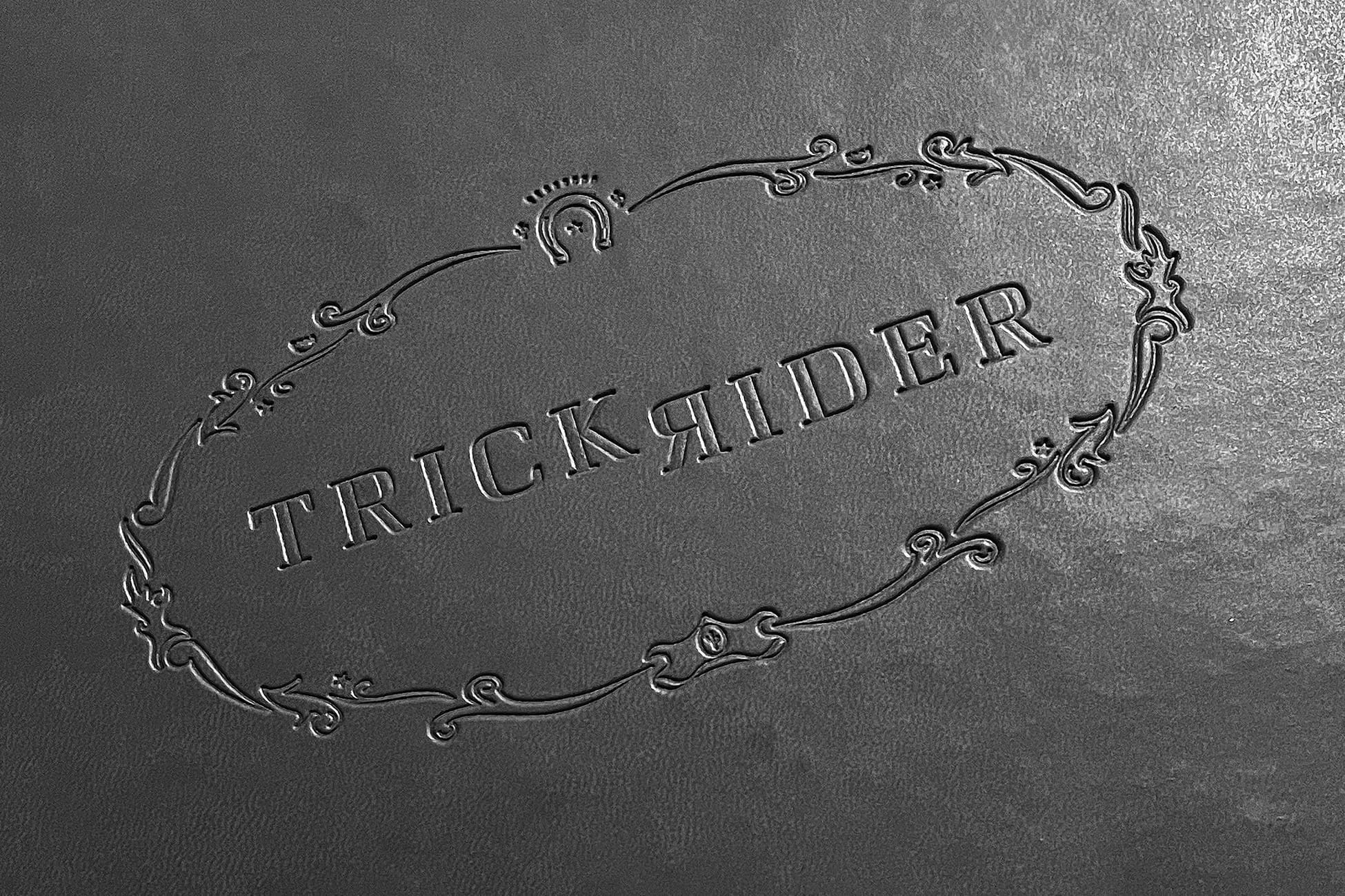 Trick Rider restaurant logo embossed on dark leather menu cover featuring ornate Victorian filigree border, horseshoe emblem, and reversed-R brand mark at Omni PGA Frisco