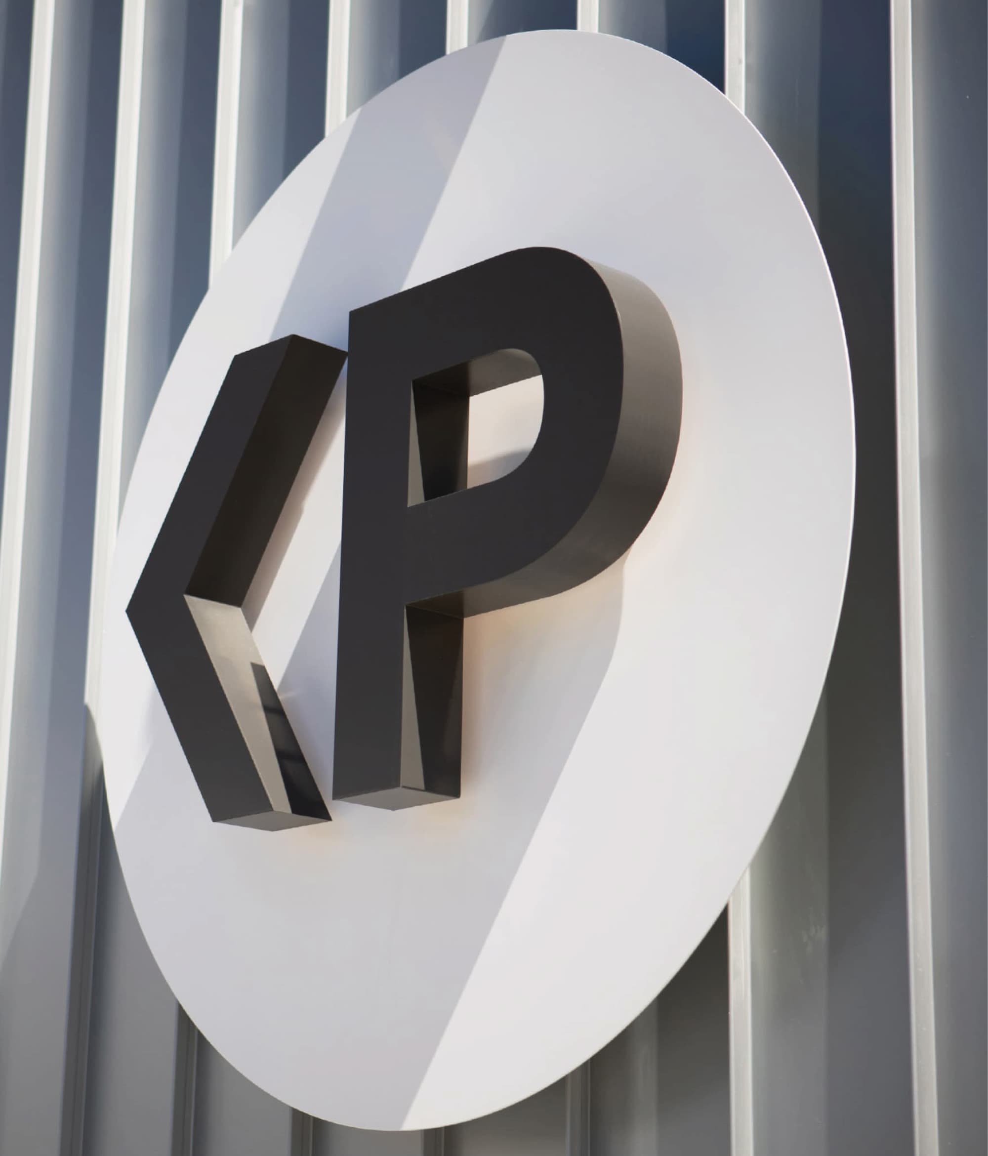 Close-up of a dimensional black parking icon with a left-pointing arrow and 'P,' mounted on a white oval sign against a corrugated metal wall.