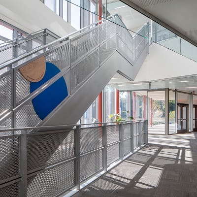 Perforated metal staircase with blue donor sign in sunlit corridor at Brentwood School campus in Los Angeles - environmental graphic design and wayfinding by RSM Design