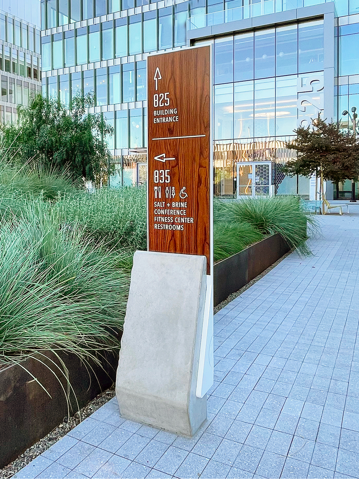 Outdoor wayfinding totem sign with wood finish and concrete base directing visitors to 825 Building Entrance and 835 Salt + Brine, Conference, Fitness Center, and Restrooms at San Carlos mixed-use development by RSM Design