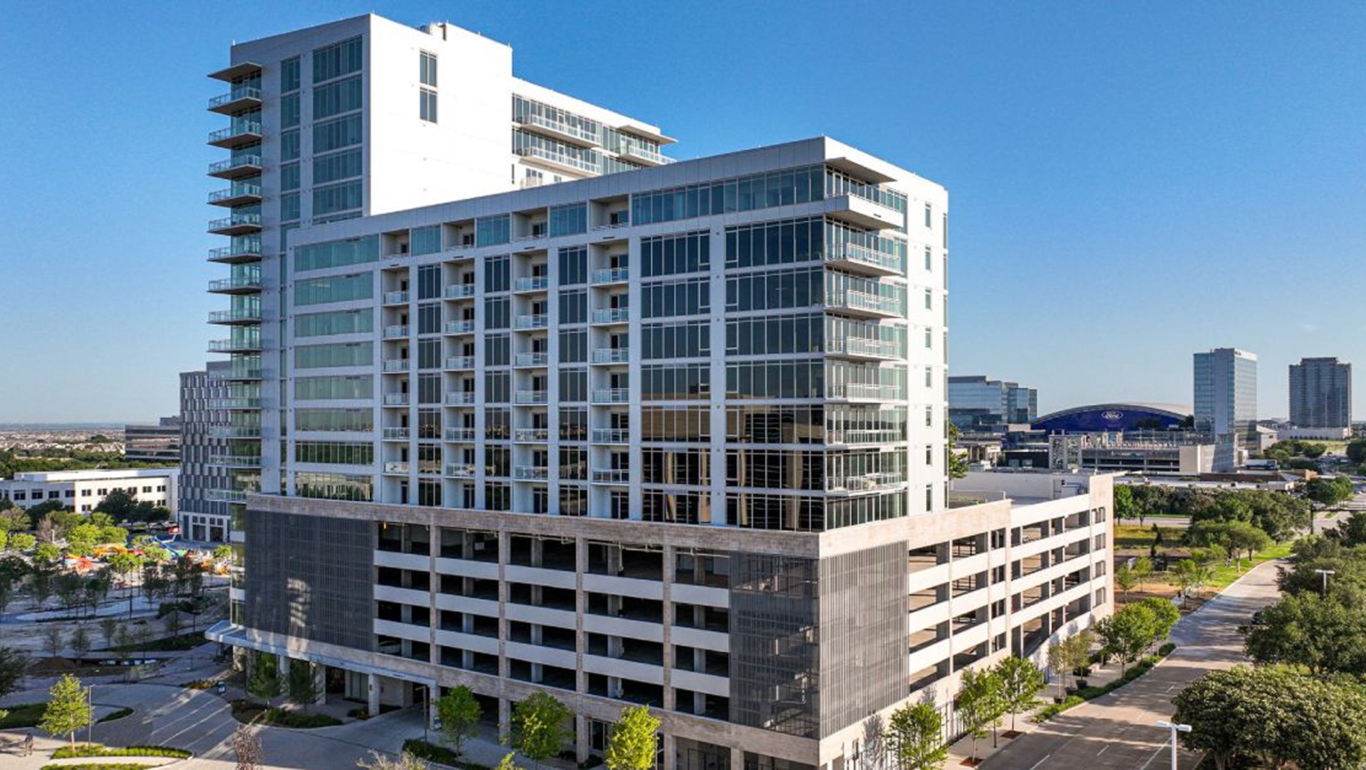Alt Text:
Monarch at Hall Park luxury high-rise apartment tower in Frisco, Texas — modern glass and white facade residential development by RSM Design, with structured parking podium and panoramic views of the Dallas-Fort Worth skyline