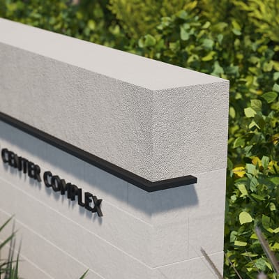 Close-up angled view of the corner edge of a textured concrete monument sign reading 'Center Complex' in black dimensional letters, surrounded by dense green foliage