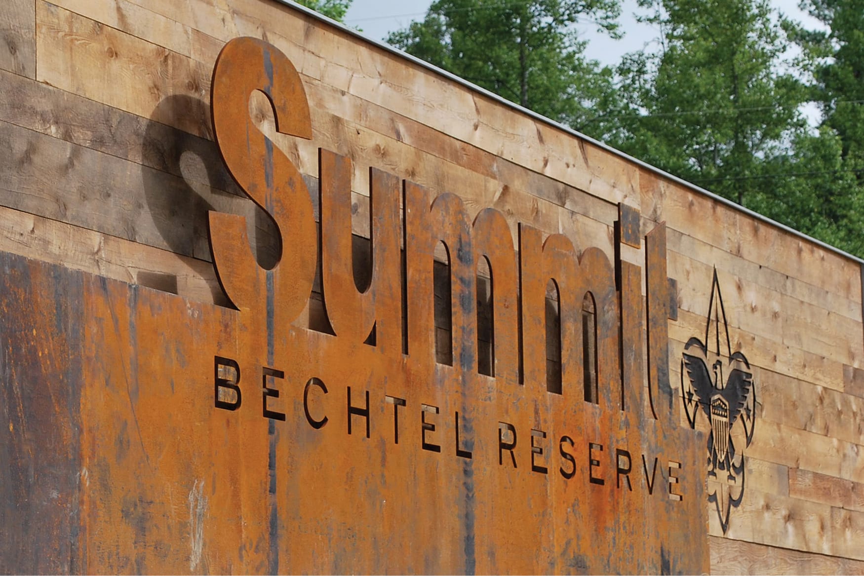 Exterior entry monument sign for Summit Bechtel Reserve with dimensional weathered steel letters and Boy Scouts of America emblem on reclaimed wood wall, placemaking signage design by RSM Design