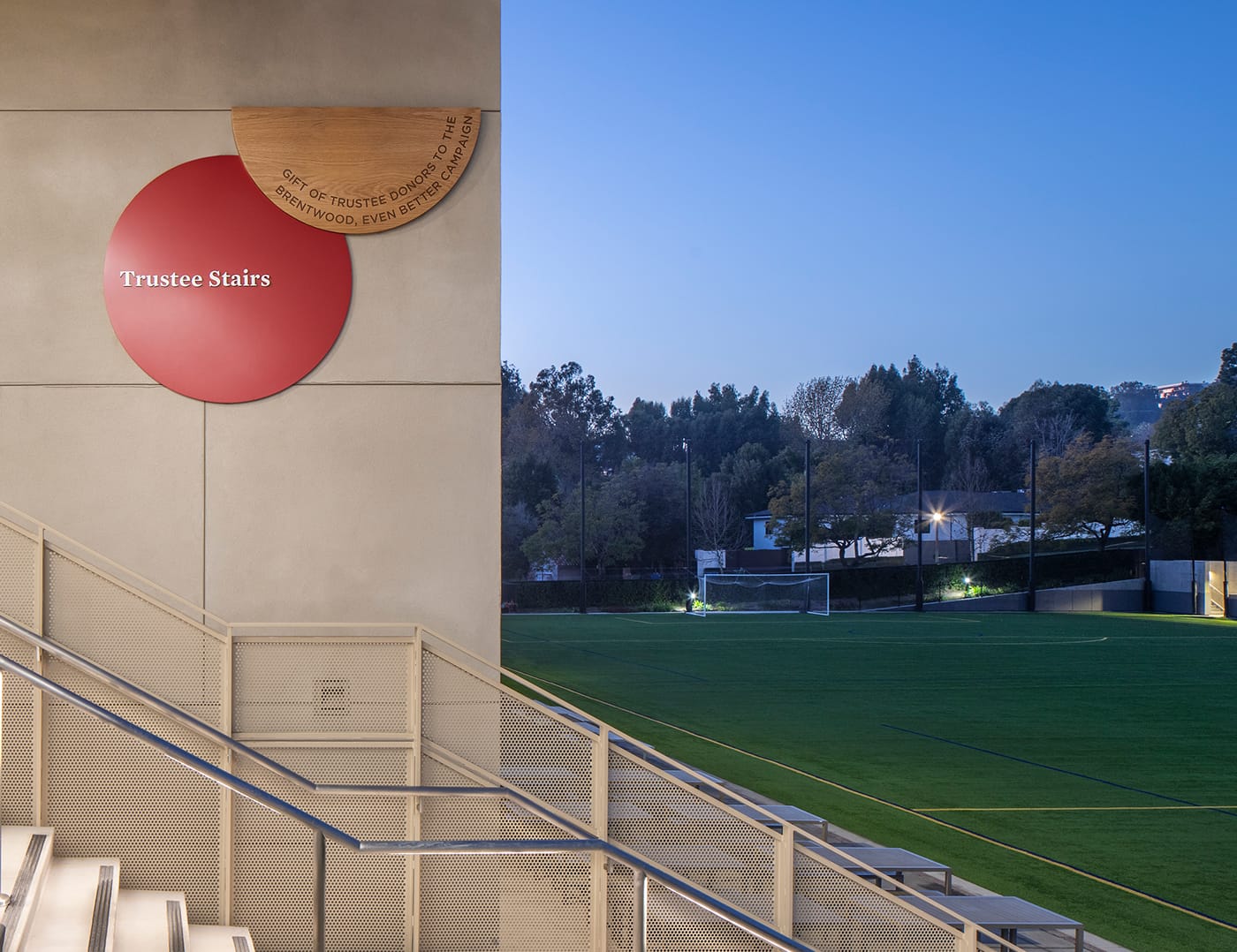 Trustee Stairs donor sign at dusk with illuminated athletic field beyond at Brentwood School campus in Los Angeles - donor recognition and environmental graphic design by RSM Design