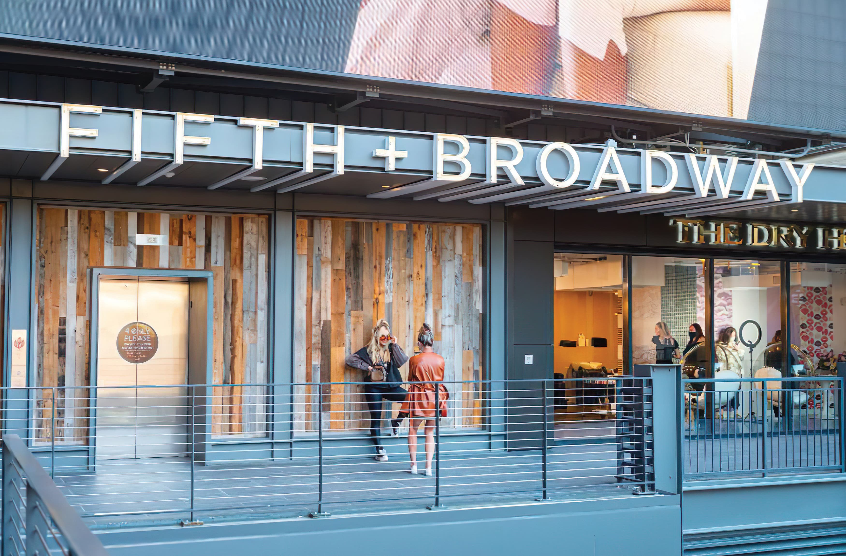 Closeup image of the Fifth + Broadway canopy identity sign in white with open channel letters, extended bottom returns of the letters to the length of the awning and neon tube lighting. Signage and wayfinding for Fifth + Broadway in Nashville, Tennessee by RSM Design