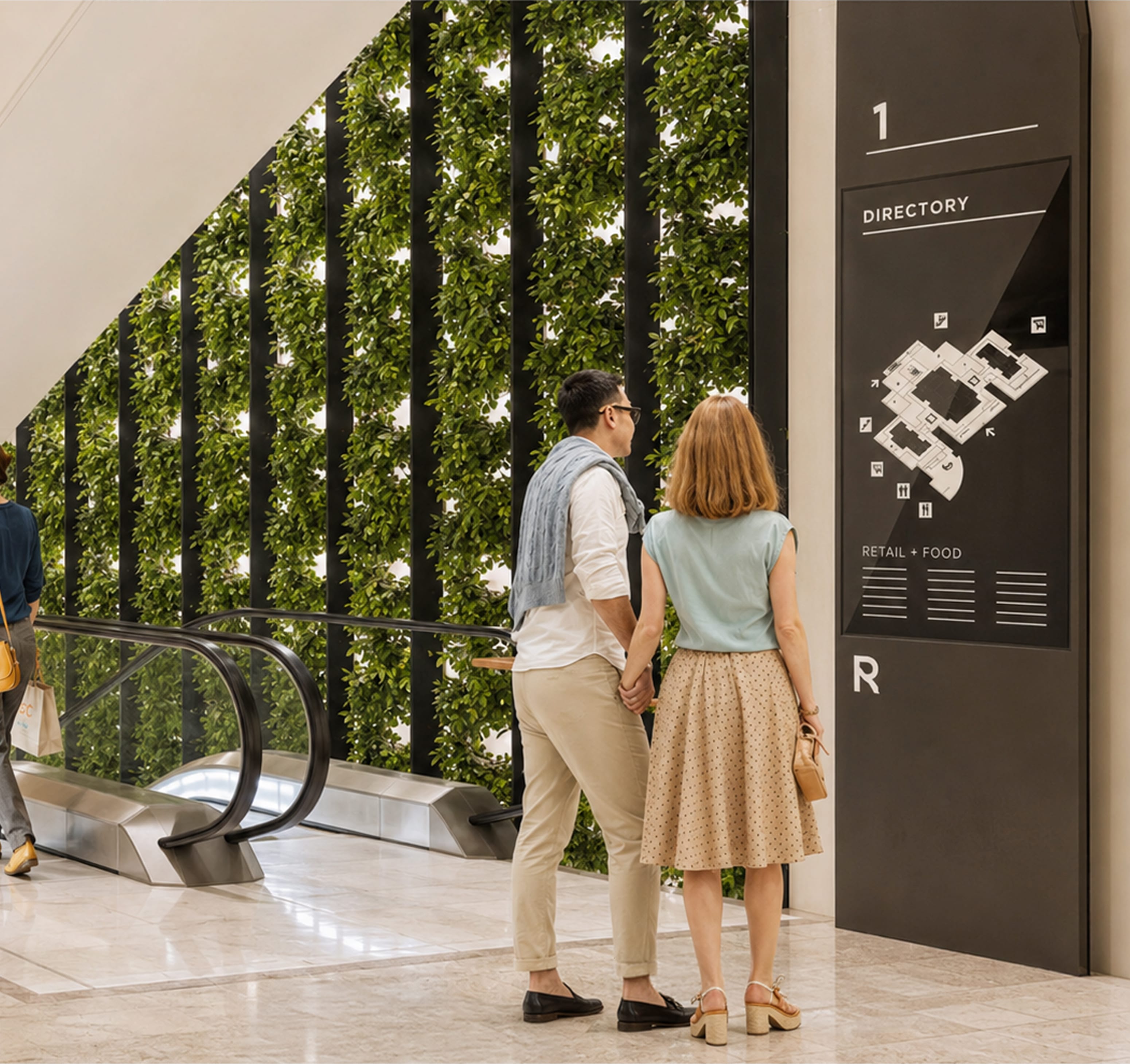 Couple viewing a level one directory sign with floor plan map and retail and food listings, escalator and living green wall behind them — wayfinding design by RSM Design