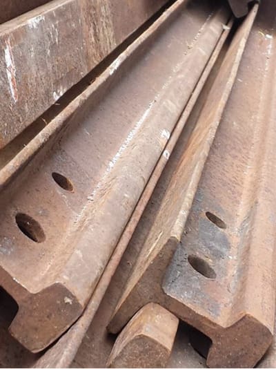 Close-up of stacked weathered steel railroad rails with bolt holes, showing rust and patina from age and use.