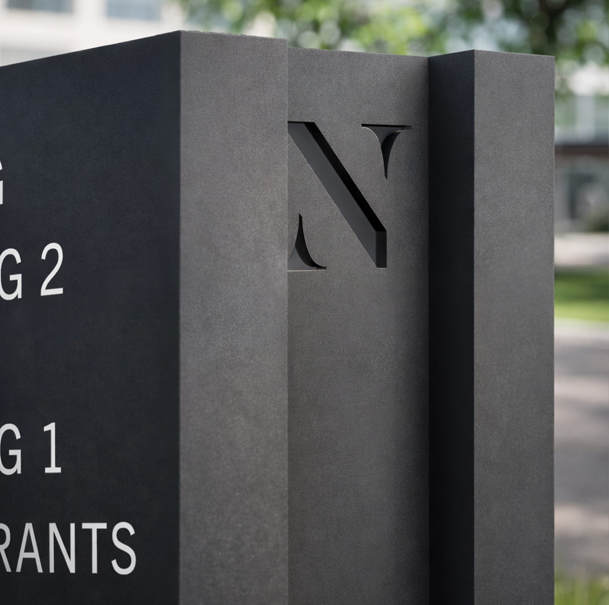 Close-up detail of a dark charcoal vehicle directional sign for The North Rim featuring a dimensional routed "N" logomark at the top and white wayfinding text indicating buildings and restaurants, showcasing RSM Design's wayfinding and signage design and master sign programs integrated into a workplace and mixed-use environment