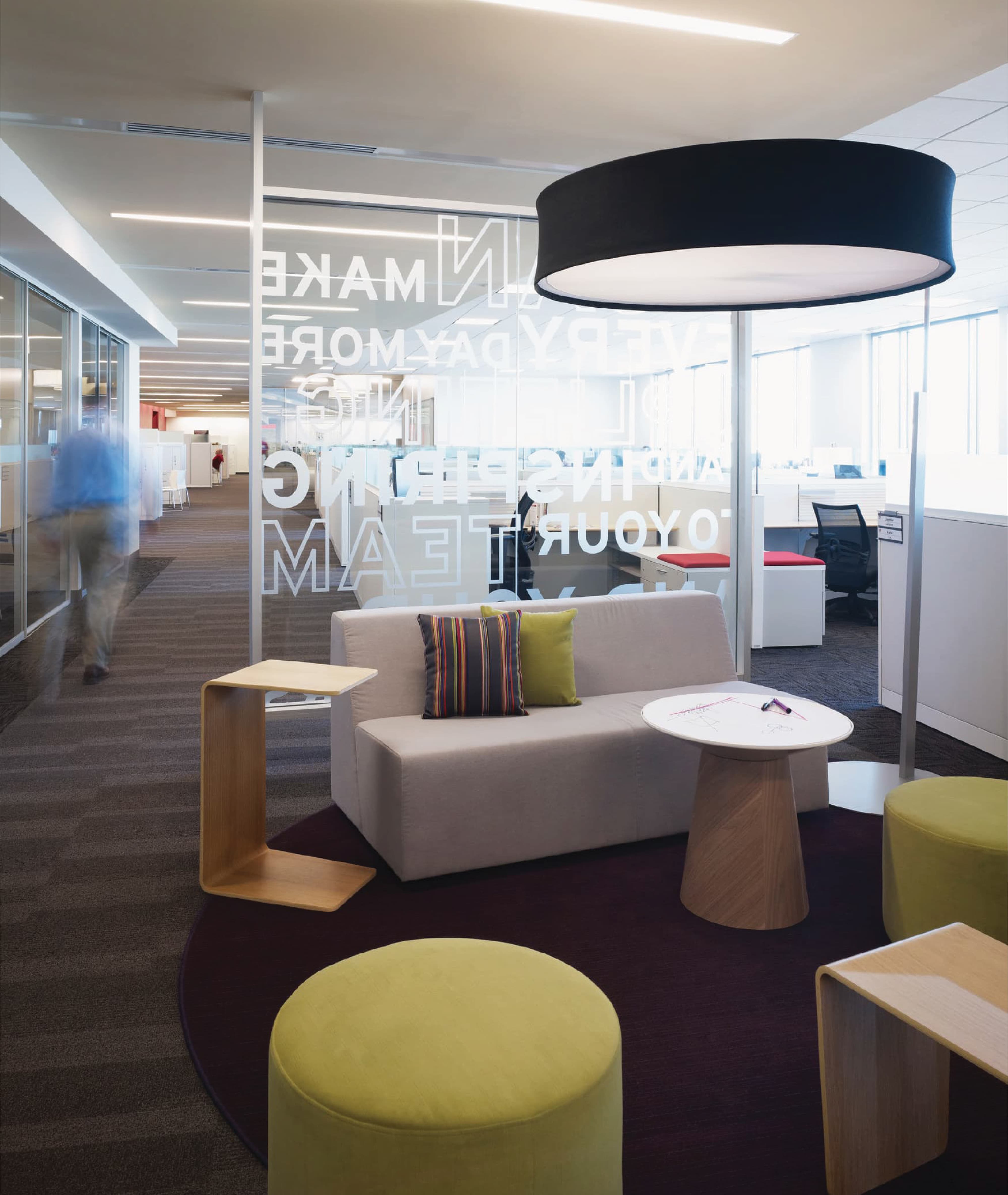 Modern corporate workplace interior with collaborative seating area and glass wall environmental graphics, illustrating branded environments, experiential graphic design, and placemaking within an open office and workplace design setting.