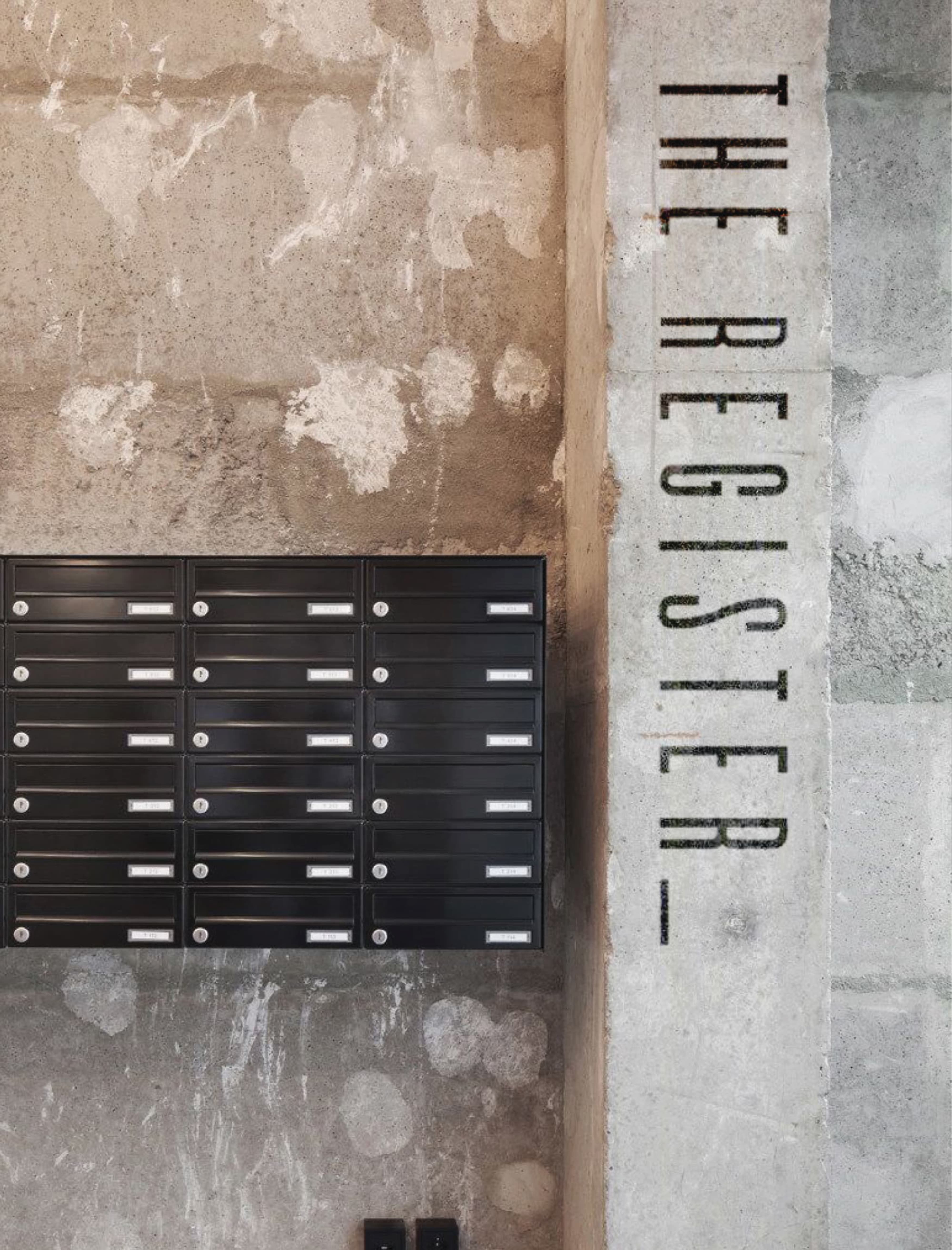 Interior lobby detail at The Register at Post District in Salt Lake City, featuring vertically stenciled brand typography directly applied to a raw concrete column alongside a residential mailbox bank — an example of RSM Design's architectural graphics and specialty graphic design seamlessly integrated into a mixed-use residential environment.