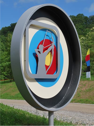 Dimensional circular archery activity sign with layered target design and archer silhouette pictogram at Summit Bechtel Reserve, sculptural outdoor wayfinding signage by RSM Design