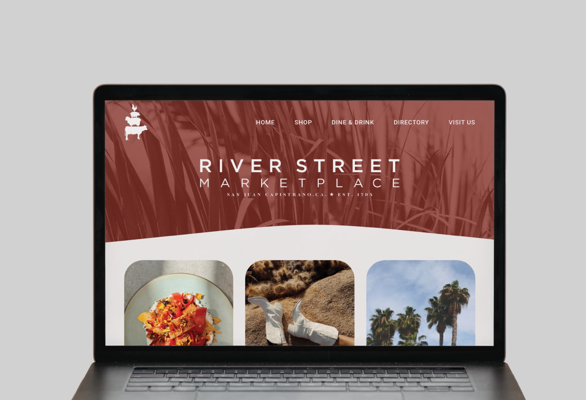 RSM Design branding and visual identity design for River Street Marketplace displayed on a laptop screen, showcasing the project's website homepage featuring the stacked farm animal logo, deep red color palette, and lifestyle imagery, demonstrating how print and digital collateral and digital integration extend a cohesive branded environment and placemaking identity across touchpoints for a mixed-use food and beverage and retail market.