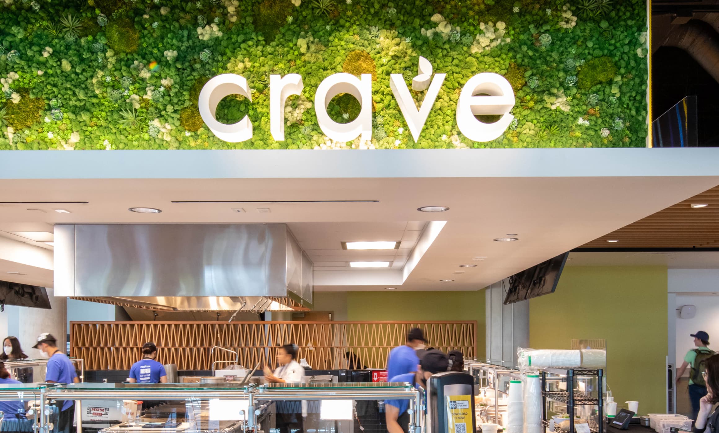  Straight on view of "crave" primary identity in white pin mounted to green plant wall in UC San Diego Sixth College's dining hall by RSM Design in San Diego, California.