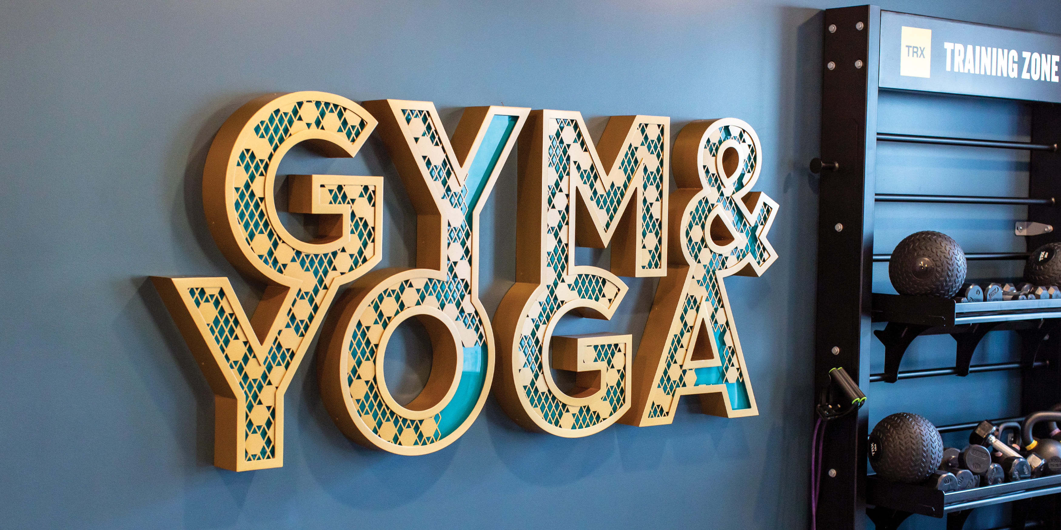 Interior Gym & Yoga amenity identity. Gold channel letters with cut out hexagonal patterned face to reveal inner teal letter face pin mounted to wall. Signage and wayfinding for Persea in San Diego, California by RSM Design