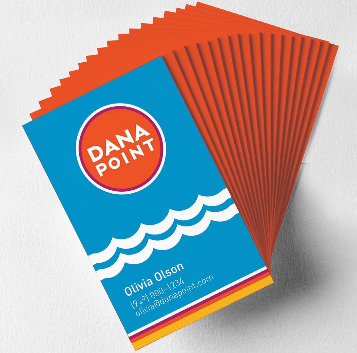 Business card mockup with the "Dana Point" circular logo and wave graphic on a blue and orange design - brand identity by RSM Design