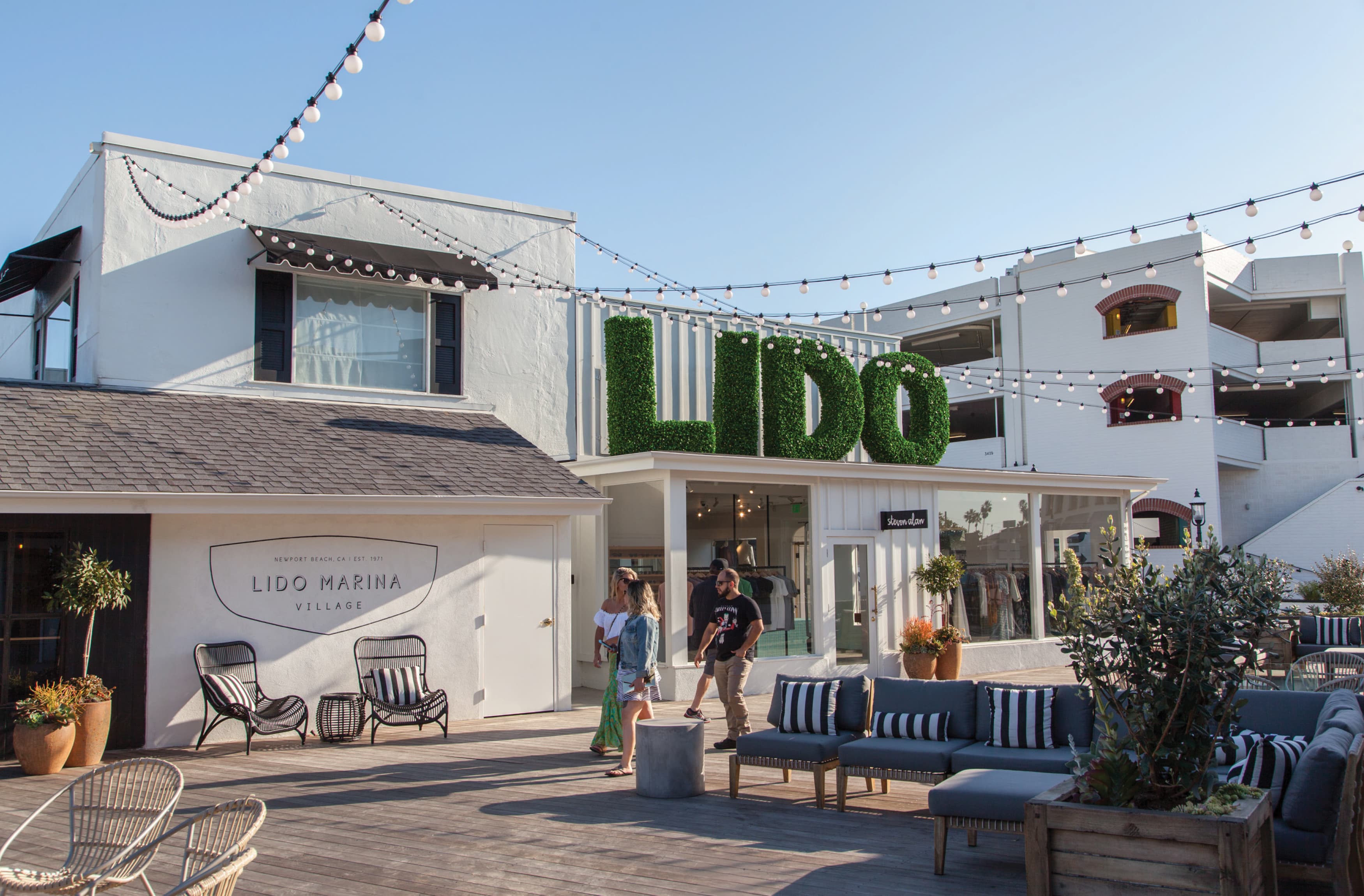 Image during the day of the plaza at Lido Marina Village with people walking about the shopping area. Lido Marina Village is an upscale waterfront destination in Newport Beach, California. 