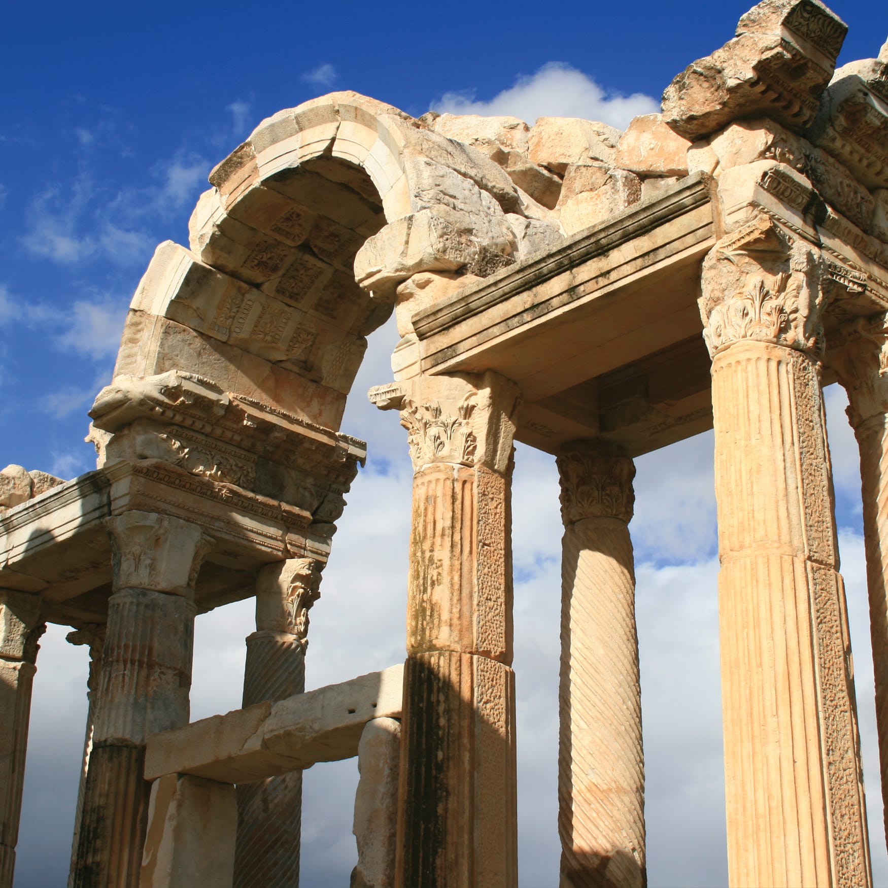 Ancient stone columns and carved arches at the Temple of Hadrian in the historical city of Ephesus, Turkey, set against a blue sky.