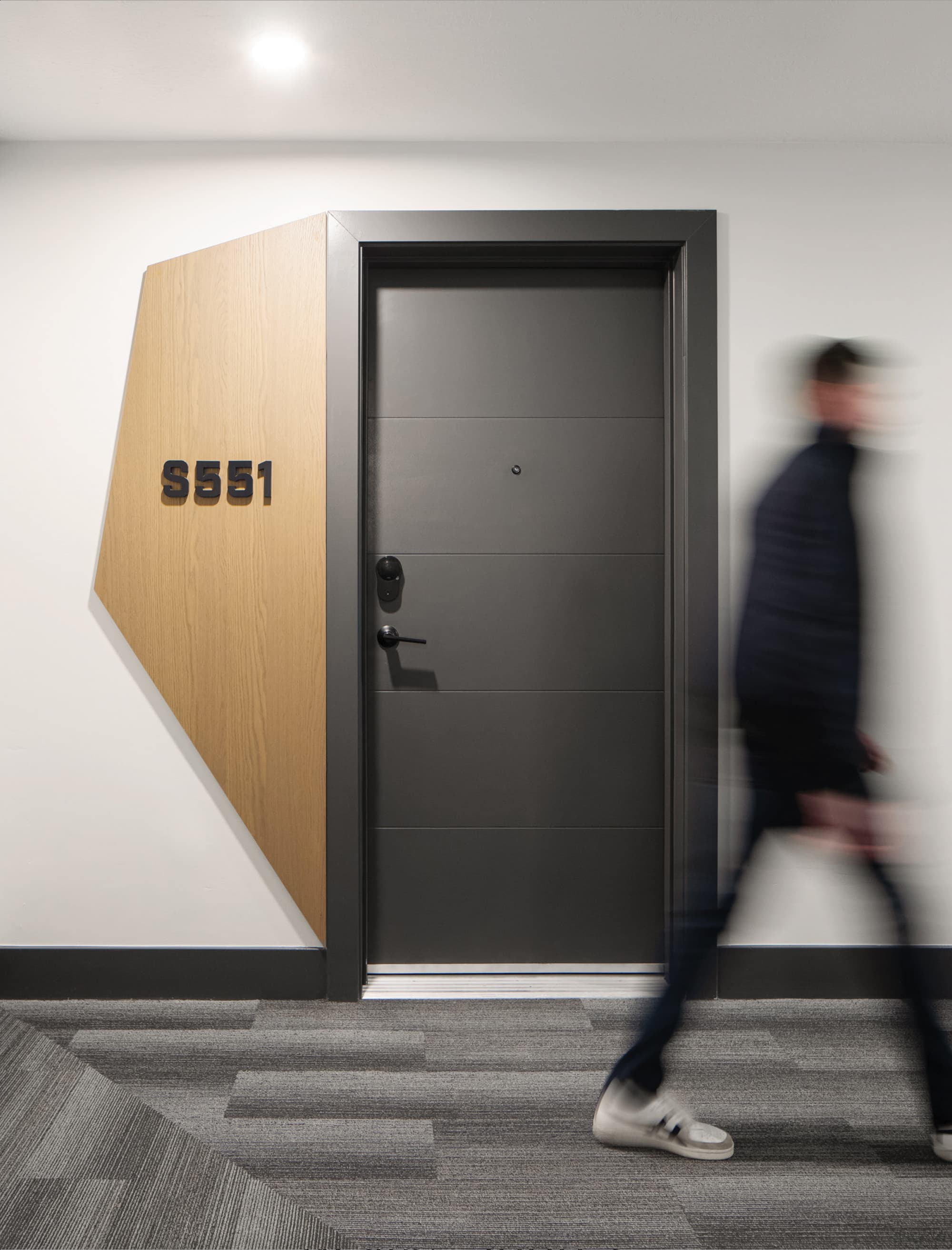 Interior residential corridor at Post District in Salt Lake City featuring a geometric wood panel unit identification sign with dimensional numerals marking apartment S551, integrated directly into the wall alongside the apartment door — showcasing RSM Design's wayfinding signage design, architectural graphics, and specialty graphic design for a mixed-use residential community.