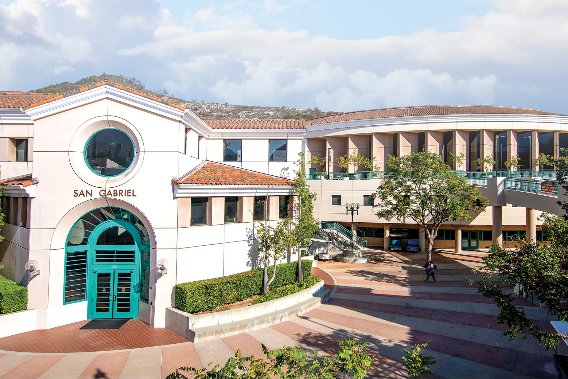 Aerial view of the San Gabriel Building at Glendale Community College, featuring Spanish Colonial architecture with terracotta roof tiles, teal arched entry doors, and open campus courtyard with San Gabriel Mountains in the background
