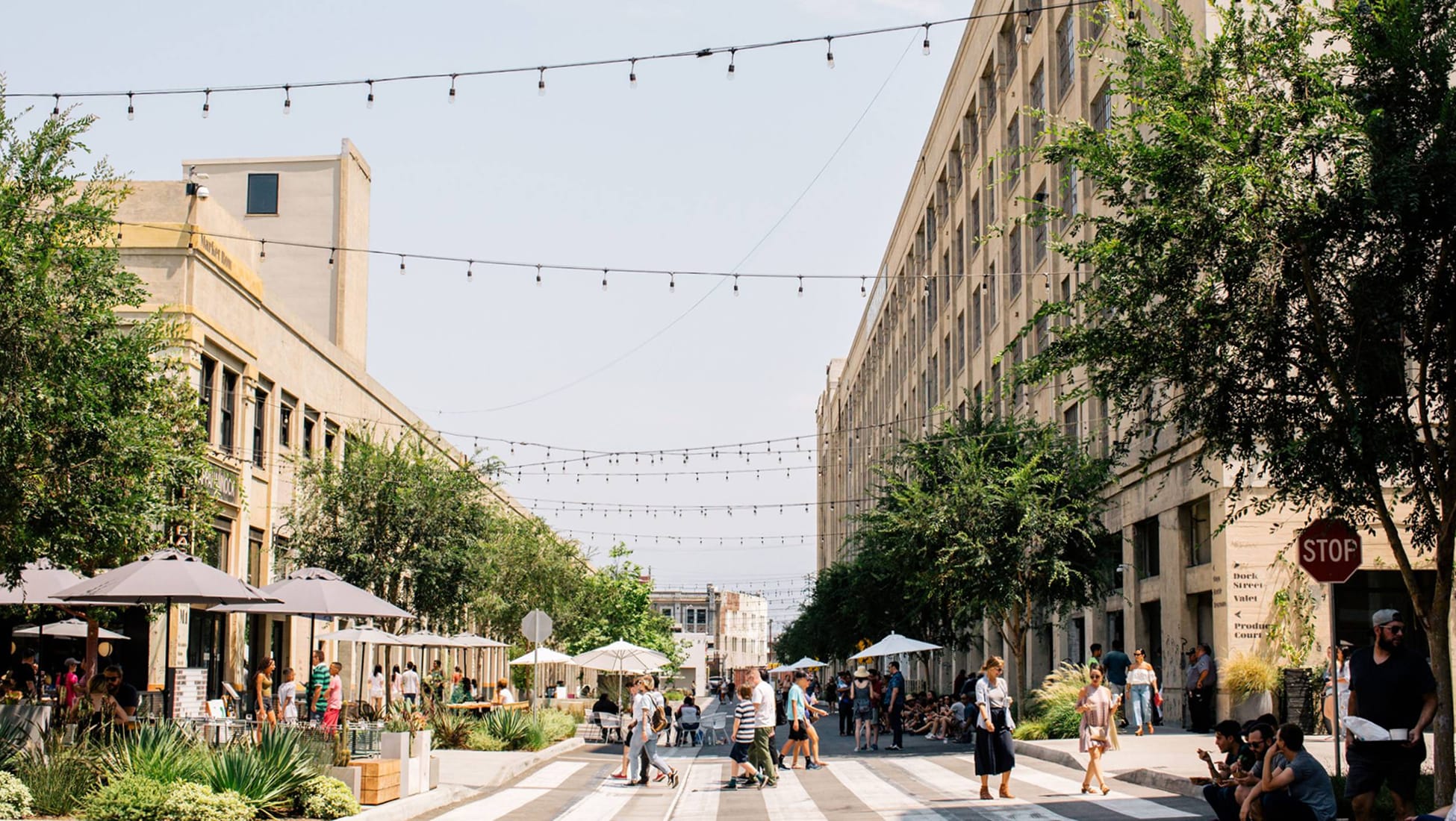 Pedestrian street lined with historic warehouse buildings, string lights, and cafe seating at ROW DTLA - placemaking and environmental graphic design by RSM Design