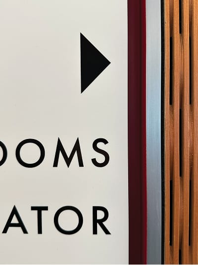 RSM Design Chapman University Rinker Campus Center Irvine — close-up detail of interior wayfinding signage typography and directional arrow against Chapman University red trim and warm wood slat wall