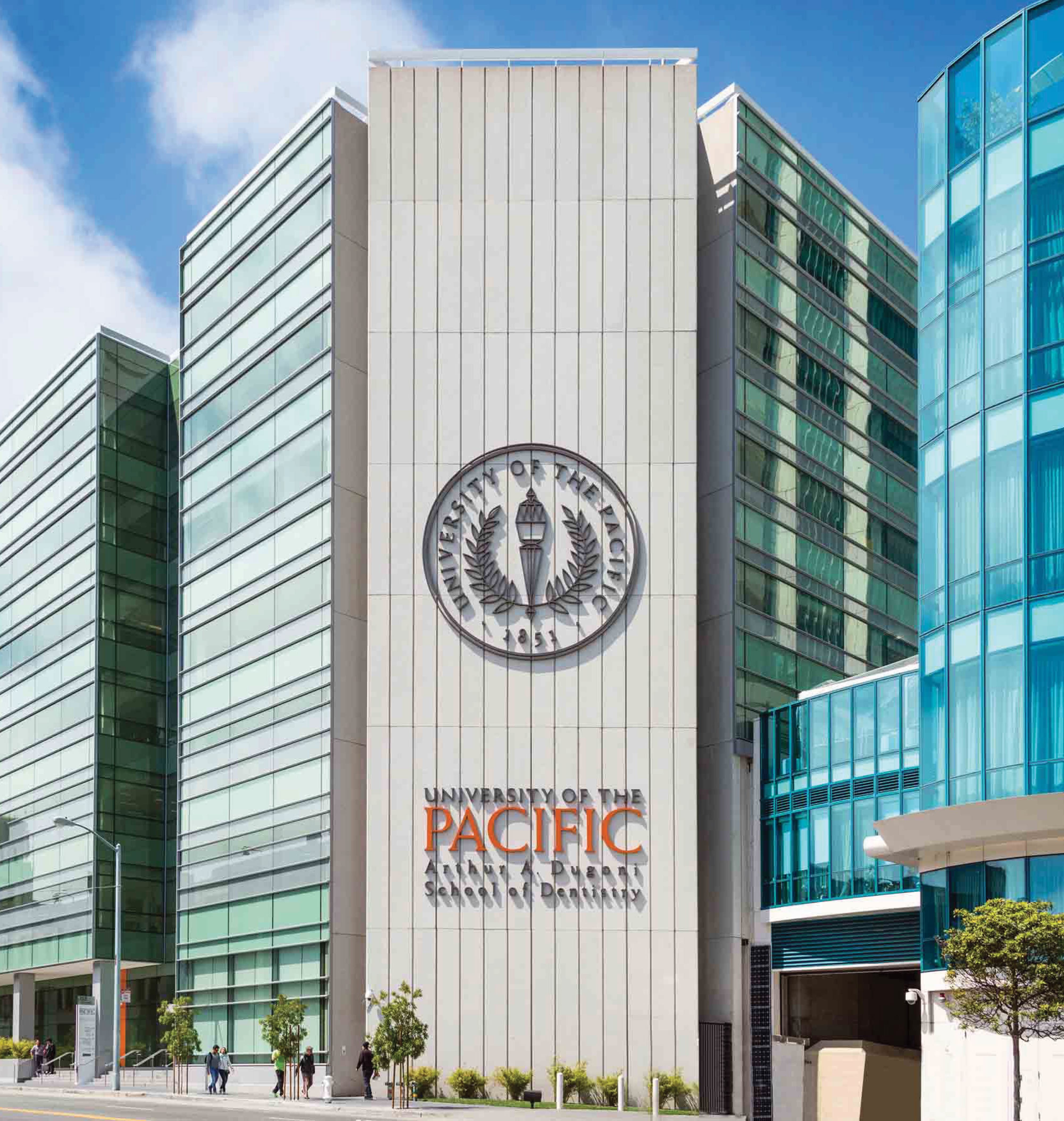 Exterior building identification signage for University of the Pacific Arthur A. Dugoni School of Dentistry featuring a large-scale dimensional university seal and bold orange institutional logotype on a white concrete tower facade in San Francisco, California — RSM Design branding and visual identity, wayfinding and signage design, master sign programs, specialty graphics, and environmental graphic design for education and health and wellness destinations.