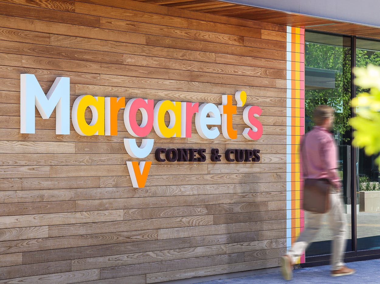 Margaret's Cones and Cups exterior dimensional signage featuring multicolor playful letters on warm wood plank wall with colorful stripe accent, ice cream shop entrance at Omni PGA Frisco