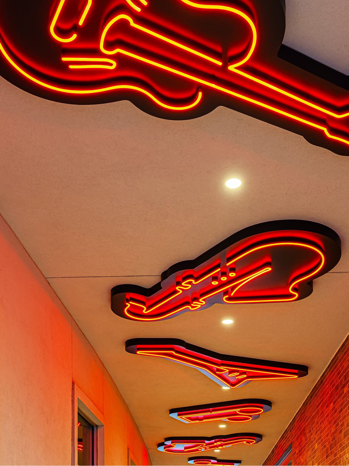 Large-scale neon guitar sculptural ceiling installations at Toyota Music Factory entertainment corridor — specialty graphics, art programs, and experiential branded environments for mixed-use and sports and entertainment destinations.
