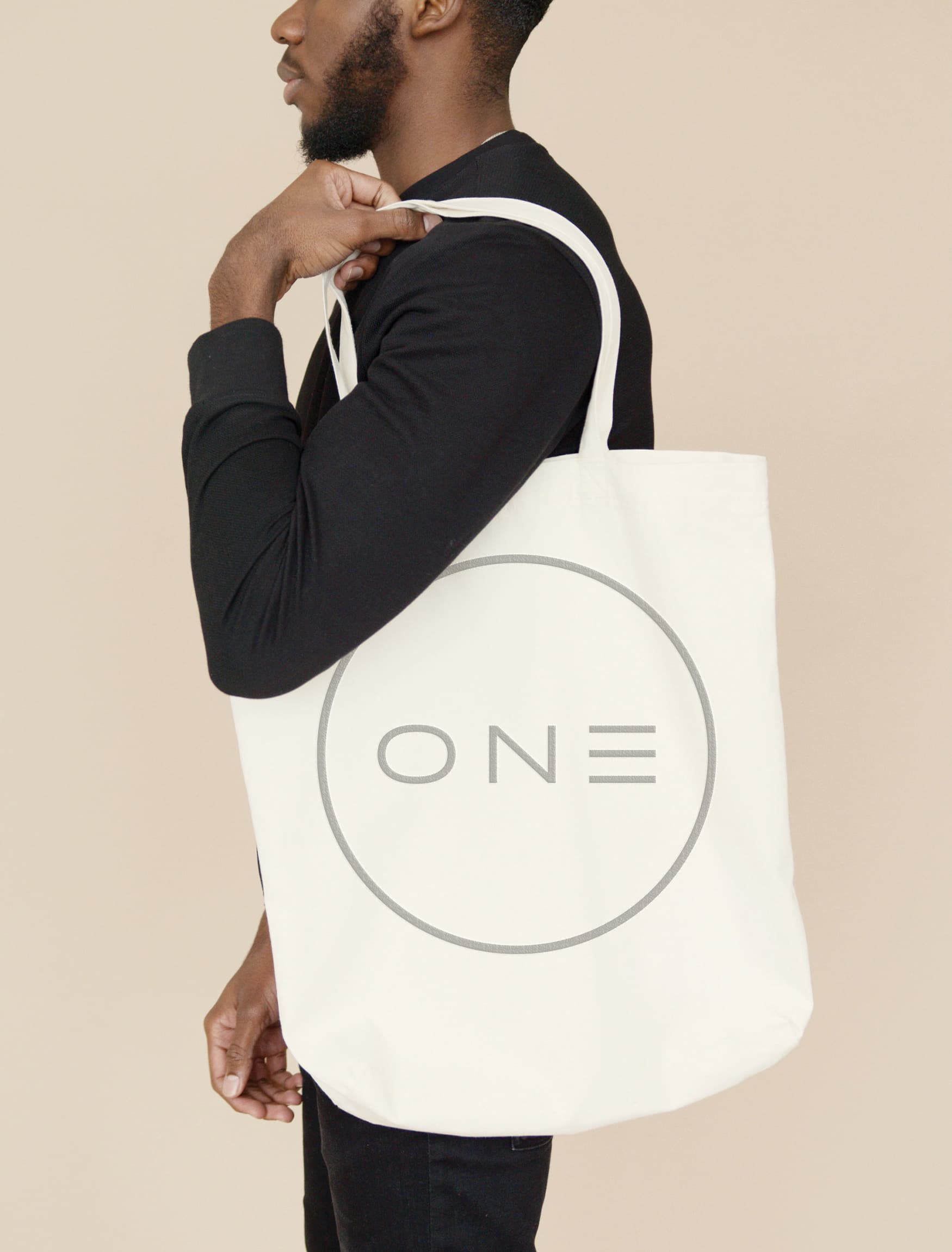 Person in front of tan wall with OneMainPlace circle logo mark tote over shoulder 