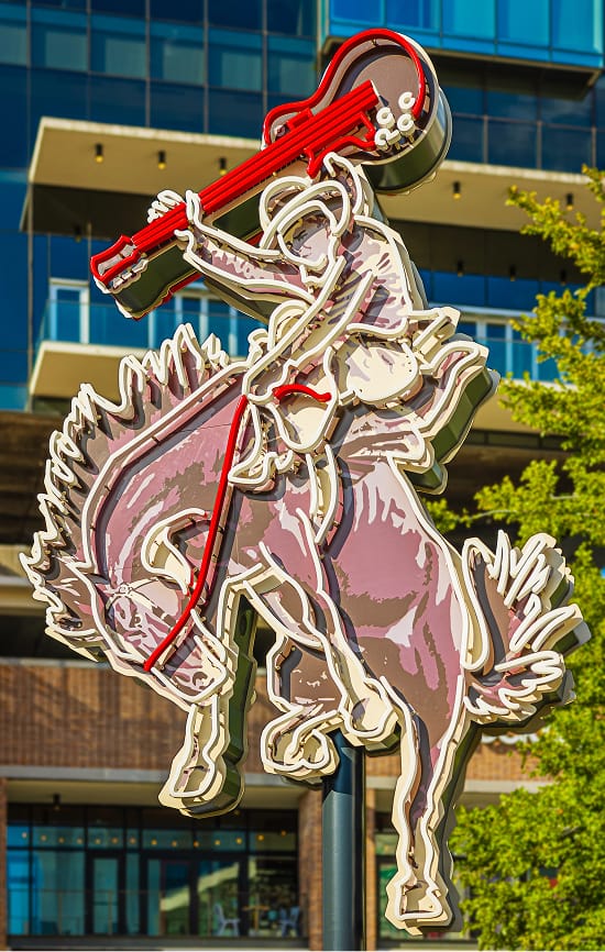 Large-scale neon cowboy and guitar sculptural landmark sign at The Music Factory mixed-use entertainment district in Irving, Texas — RSM Design specialty graphics, experiential placemaking, and branded environmental design for mixed-use, streetscape, and food and beverage destinations.