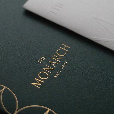 The Monarch at Hall Park brand identity close-up — gold foil stamped logo and geometric botanical pattern on deep forest green textured folder, luxury print design by RSM Design