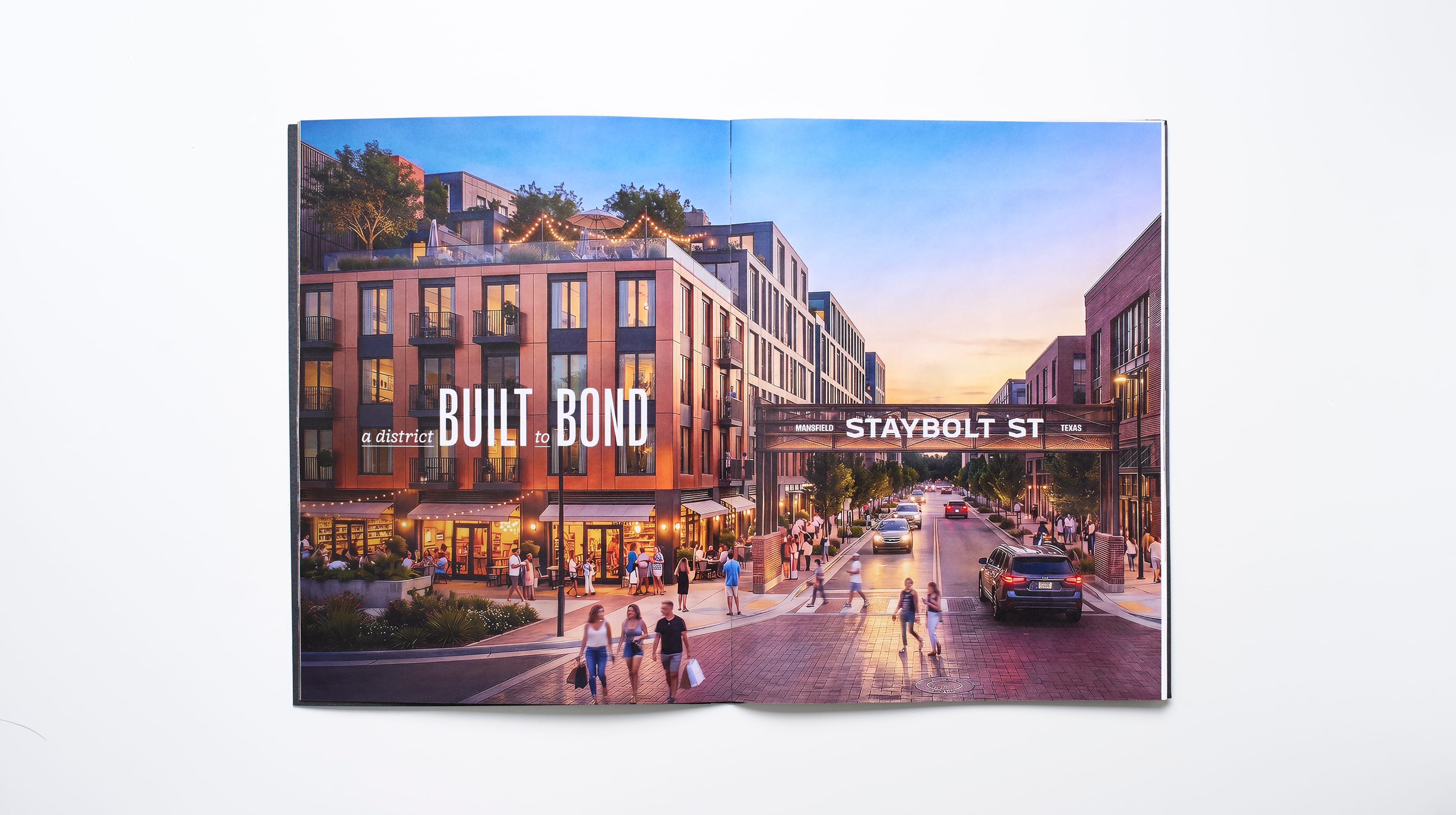 Open leasing brochure spread with a dusk rendering of a mixed-use retail street lined with brick buildings, string lights, and pedestrians, framed by a steel gateway sign reading Staybolt St, Staybolt Street, Mansfield, Texas, brand identity and leasing collateral design by RSM Design