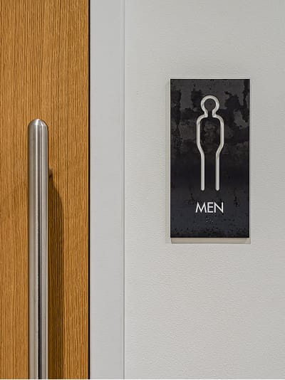Men's restroom identification sign with illuminated pictogram beside wood door at Dallas Holocaust and Human Rights Museum - ADA wayfinding signage by RSM Design