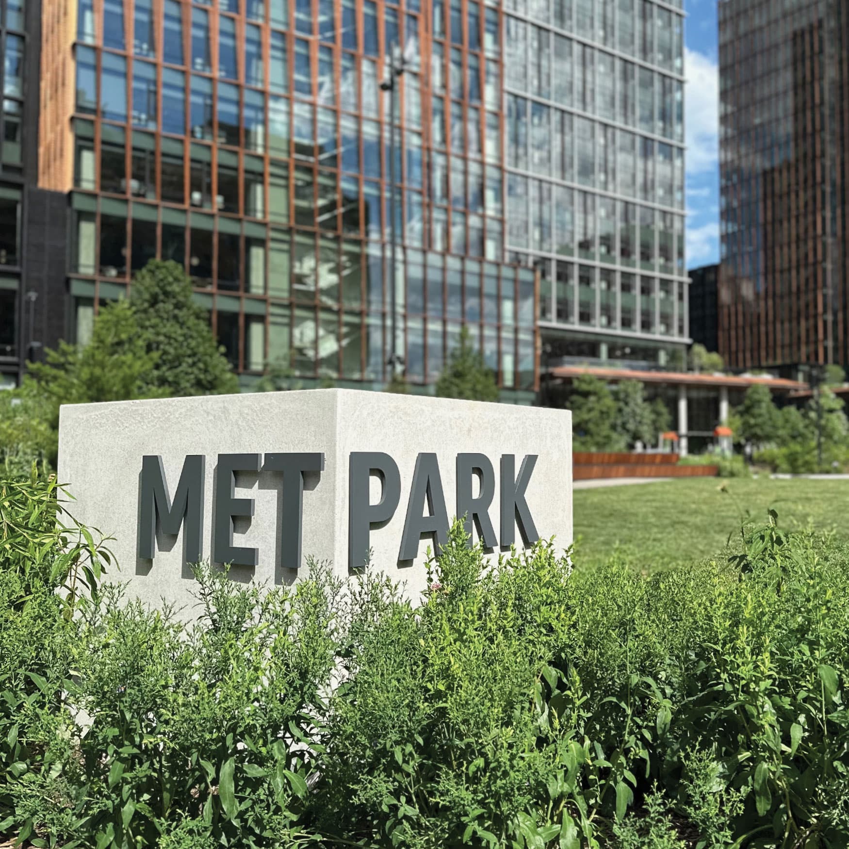 This sign appears to be a monument sign, typically used to mark the entrance of a significant location such as a park, business complex, or residential area. Monument signs are generally placed at eye level and constructed from durable materials like stone, concrete, or metal to ensure longevity and visibility. In this case, the sign for "MET PARK" is designed to be easily readable and is likely intended to designate the name of the park or the area.