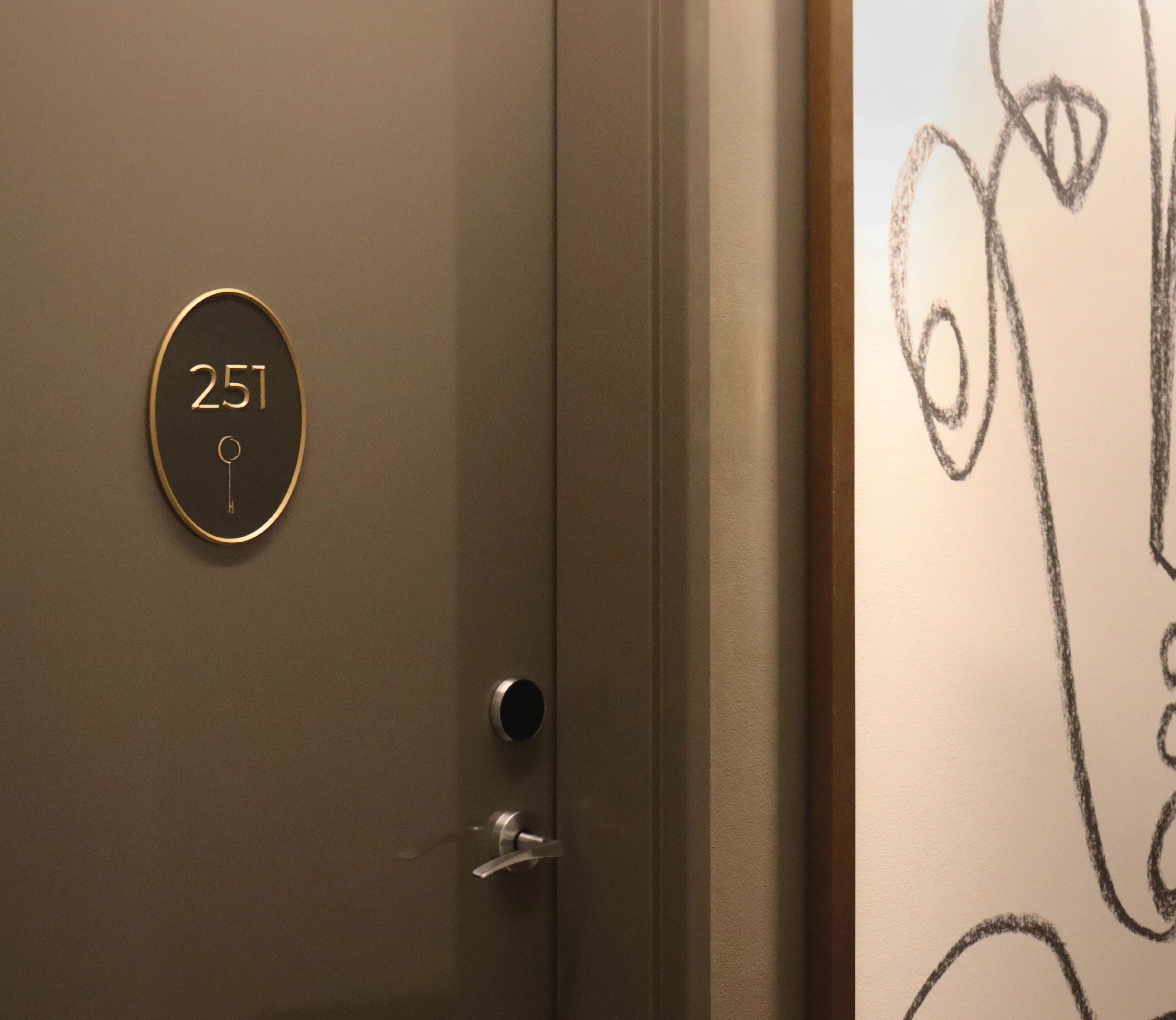 The Crescent Hotel guest room door number 251 with elegant gold oval room number plaque, keyless entry lock, and contemporary line art wall mural in the hotel corridor