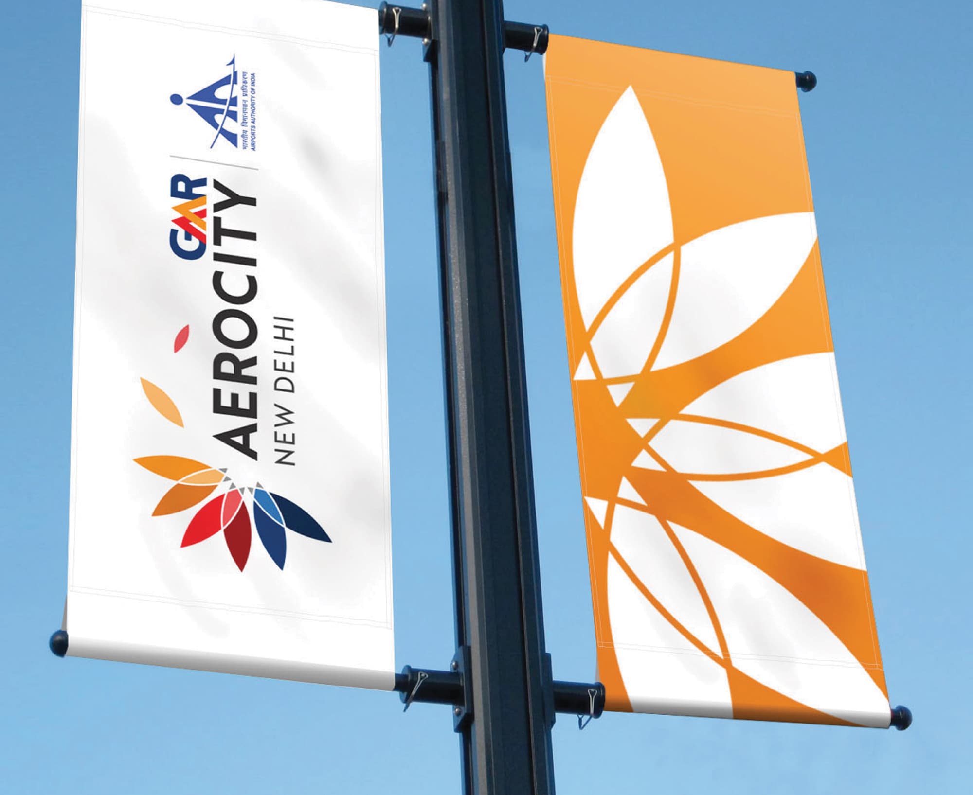 GMR Aerocity New Delhi branded streetscape light pole banners featuring the colorful lotus flower brand identity and bold orange graphic pattern against a blue sky — RSM Design branding and visual identity, print and digital collateral, experiential placemaking, and environmental graphic design for mixed-use, transit, streetscape, and international destinations.