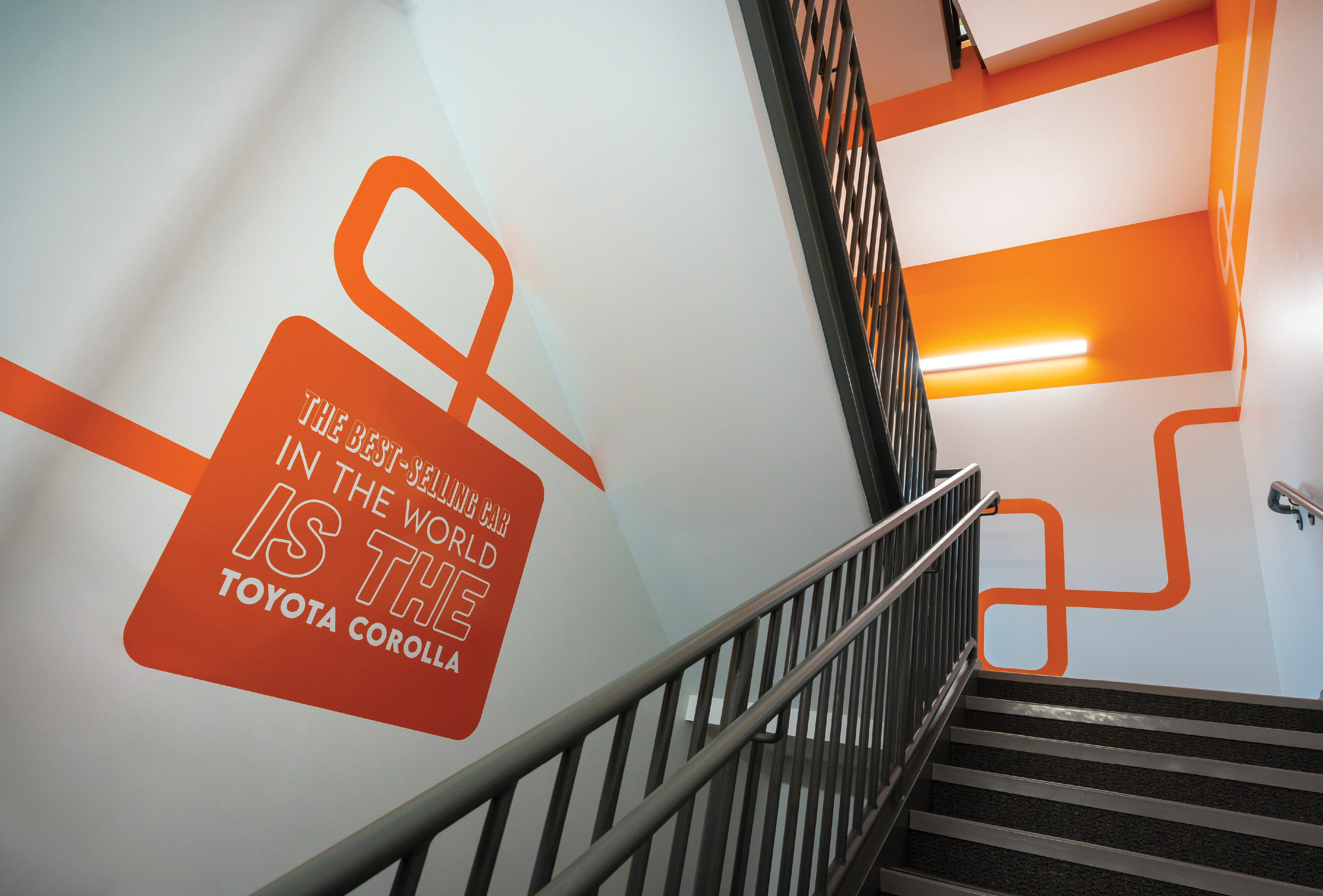 Branded stairwell environmental graphics featuring Toyota Corolla messaging and bold wayfinding lines, showcasing experiential design, brand storytelling, and placemaking within a corporate workplace and automotive innovation environment.