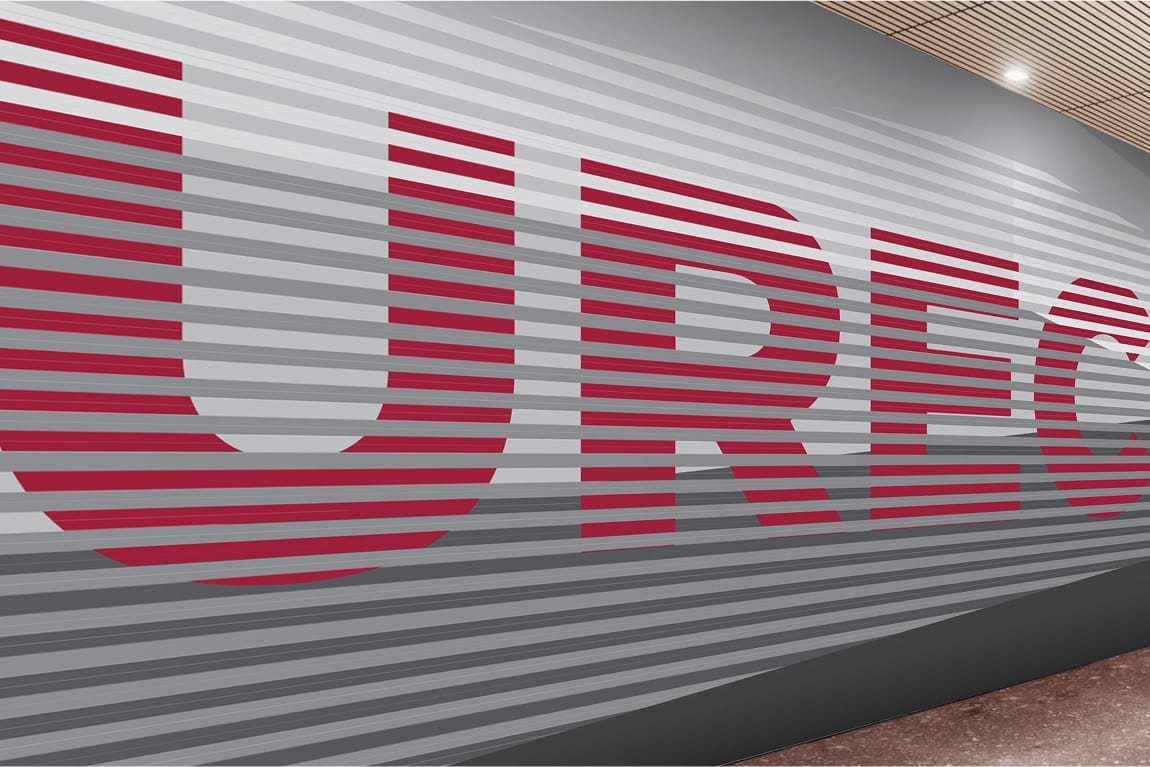Close-up of a large-scale "UREC" branded accent wall featuring bold crimson letters layered over a ribbed gray panel surface, creating a dimensional striped effect. A wood-slat ceiling and polished floor are visible at the edges of the frame.
