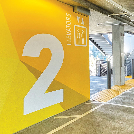 Bold yellow level 2 elevator wayfinding wall graphic in parking structure at 825-835 San Carlos, interior parking garage signage and environmental graphic design by RSM Design