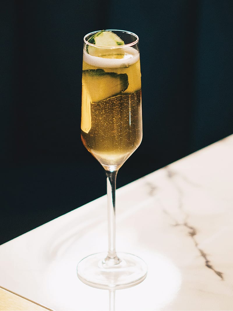 Champagne flute cocktail with cucumber garnish on marble table at Trick Rider, Omni PGA Frisco Resort, brand identity lifestyle imagery by RSM Design.