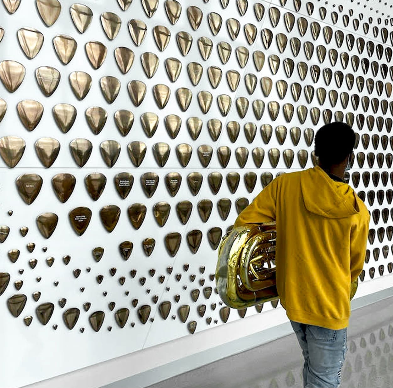Student holding a tuba examining engraved bronze guitar pick donor wall art installation at the Buddy Holly Hall of Performing Arts and Sciences, Lubbock Independent School District, Lubbock Texas