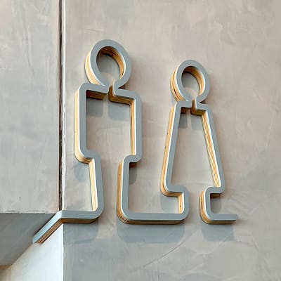 Contemporary brushed gold and gray restroom signage with minimalist male and female figure icons mounted on a textured concrete wall at the Buddy Holly Hall of Performing Arts and Sciences, Lubbock Texas