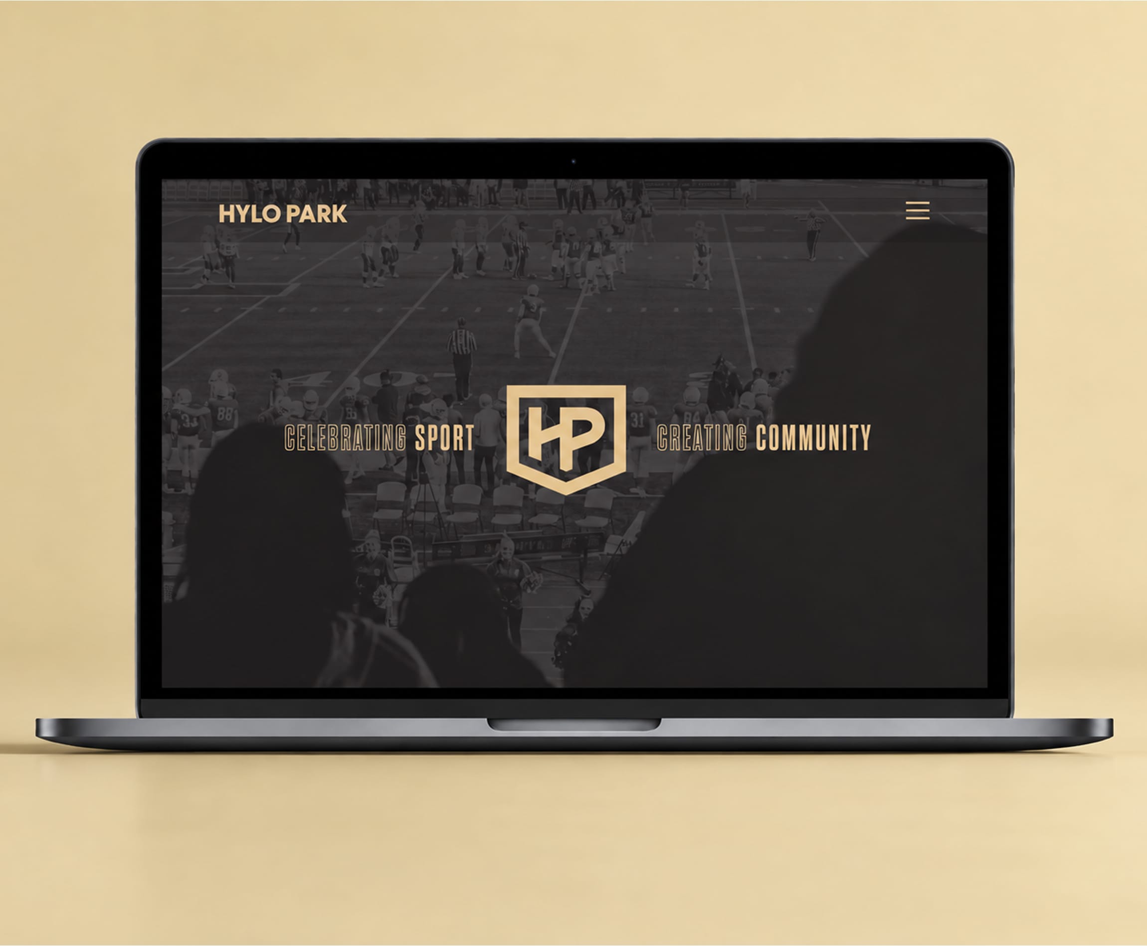 Laptop showing the Hylo Park website homepage, with the gold HP shield monogram and the line Celebrating Sport, Creating Community over a dark photo of a youth football game, Hylo Park, Las Vegas, brand identity design by RSM Design.