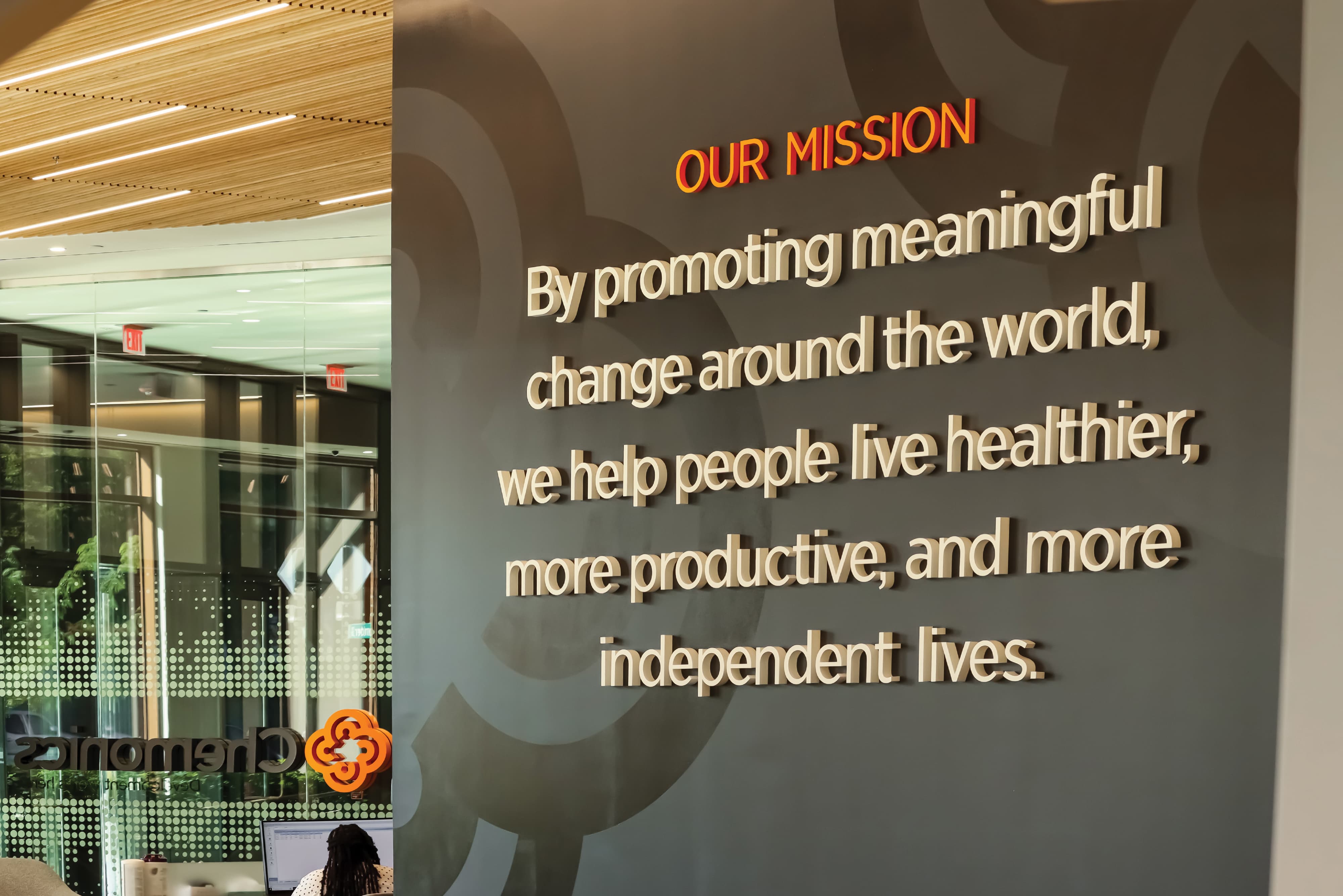 Interior branded mission wall with dimensional lettering and integrated graphics, showcasing environmental graphic design, experiential graphics, and brand storytelling for corporate workplace, healthcare, and commercial environments.