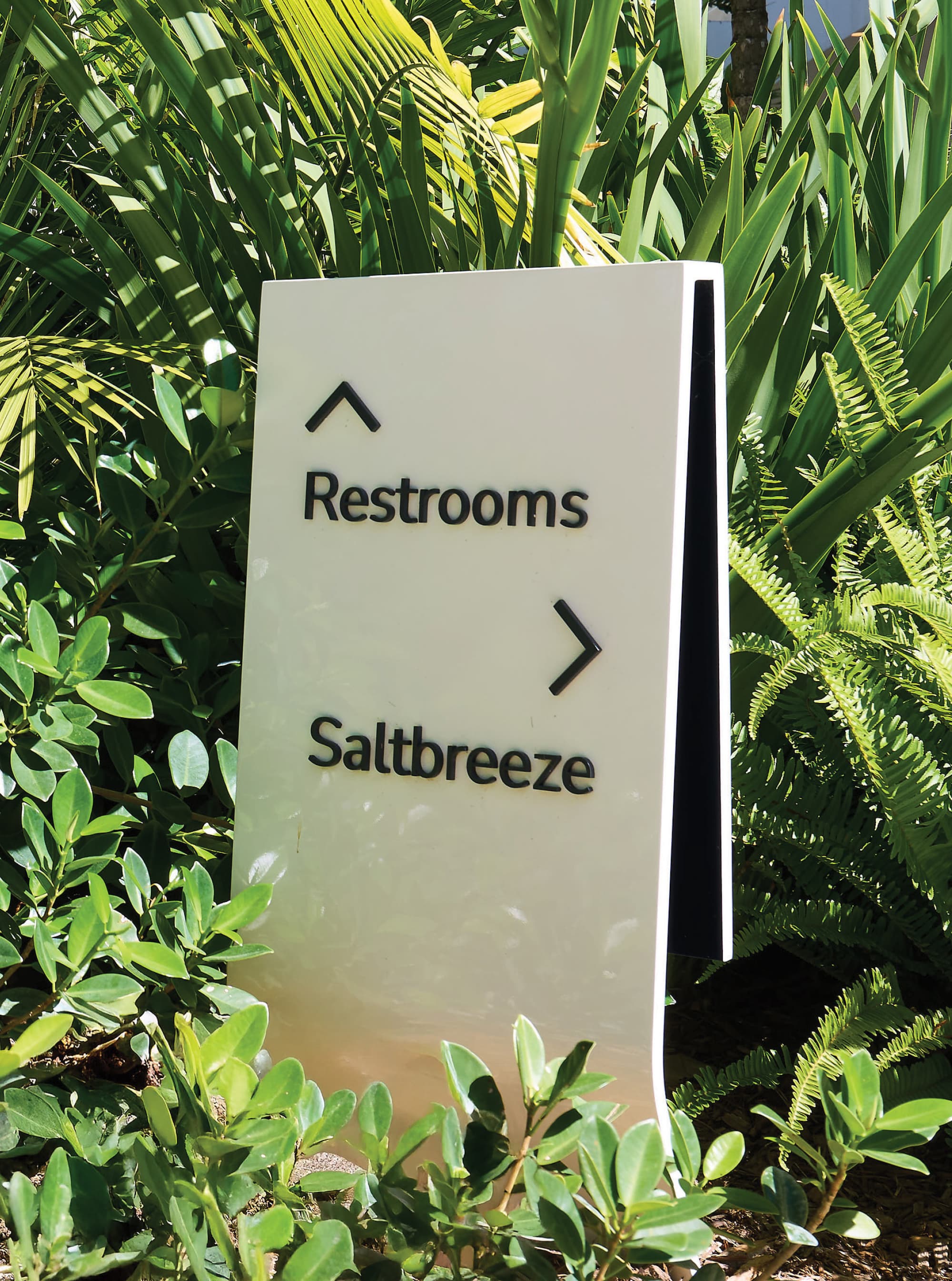Exterior pedestrian wayfinding sign directing guests to restrooms and Saltbreeze restaurant amid tropical landscaping at Pier Sixty-Six luxury waterfront resort in Fort Lauderdale, Florida — RSM Design wayfinding and signage design, master sign programs, and environmental graphic design for hospitality and waterfront destinations.