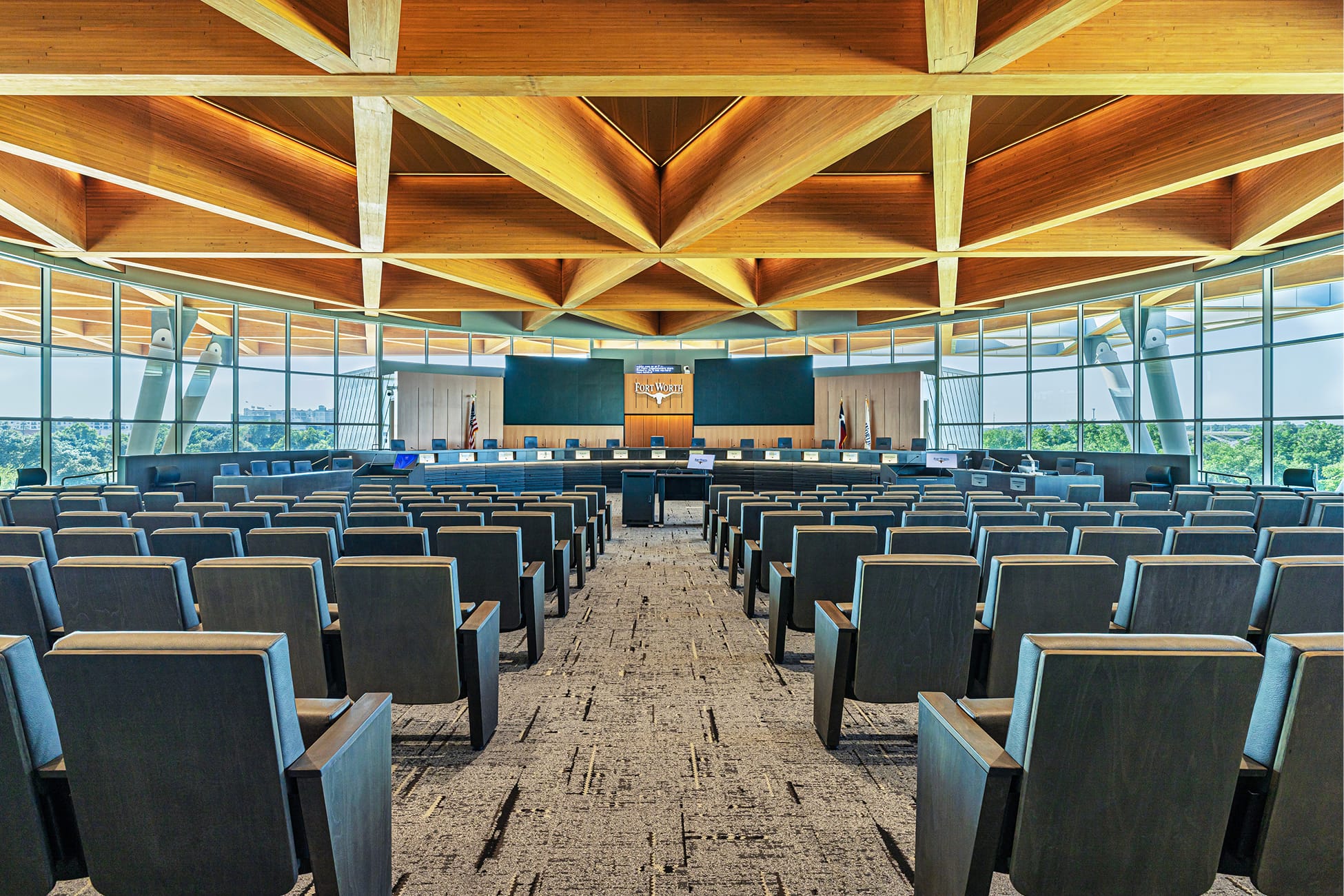 Fort Worth City Hall Council Chamber interior featuring dramatic wood lattice ceiling, floor-to-ceiling glass walls with city views, curved dais with Fort Worth longhorn logo, and rows of public seating