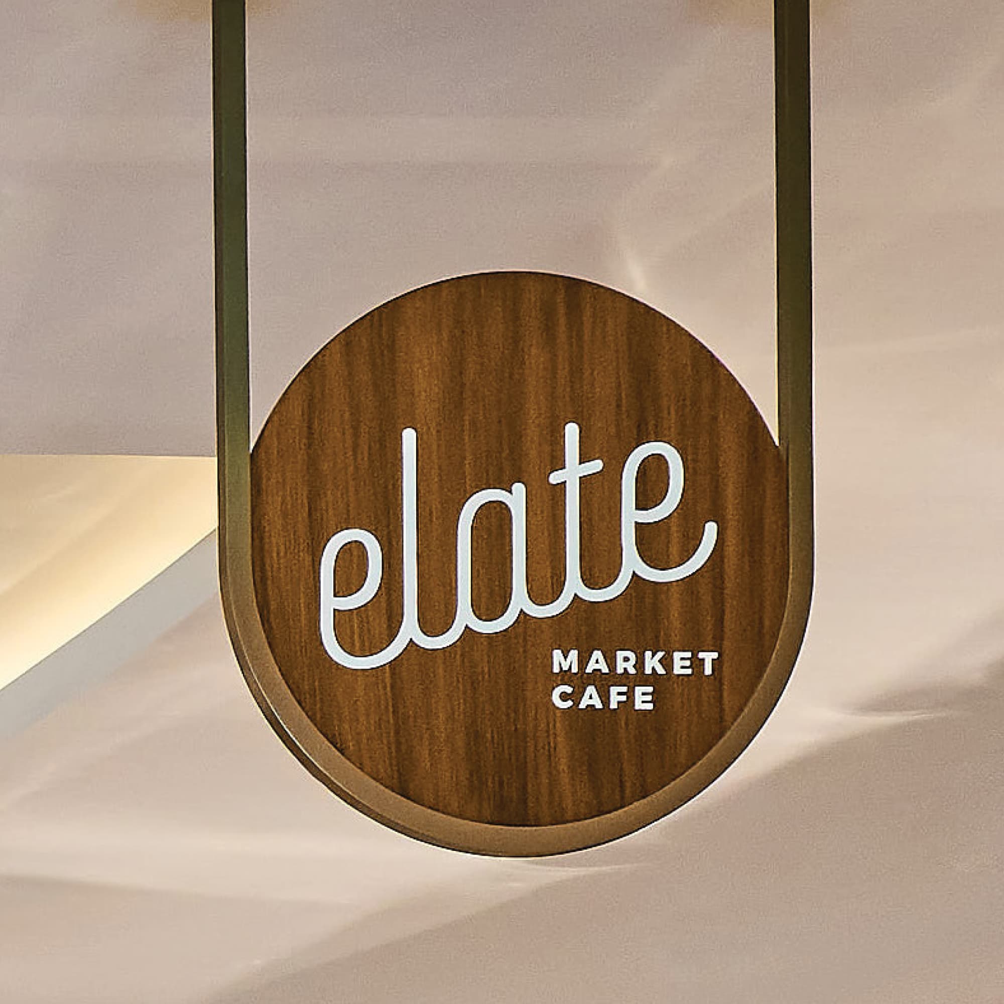 Circular suspended wood and brass tenant identification sign for Elate Market Cafe with script logo typography at Pier Sixty-Six luxury waterfront resort in Fort Lauderdale, Florida — RSM Design branding and visual identity, wayfinding and signage design, specialty graphics, and branded environments for hospitality, food and beverage, and waterfront destinations.