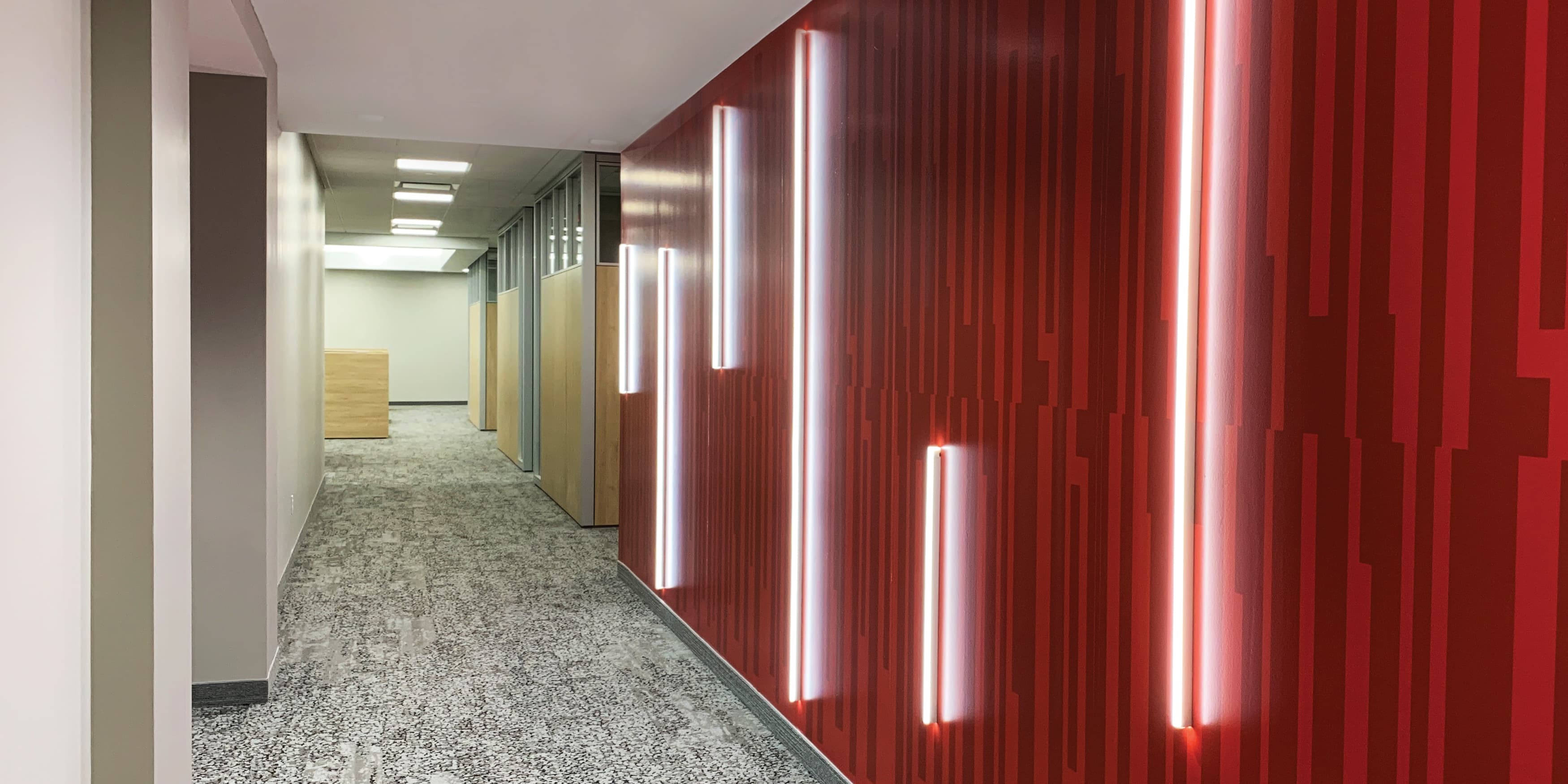 Speciality art mural by RSM Design for JMFE Headquarters consisting of red vertical painted lines in a pattern with red neon line art signage overlaying for office workplace design.