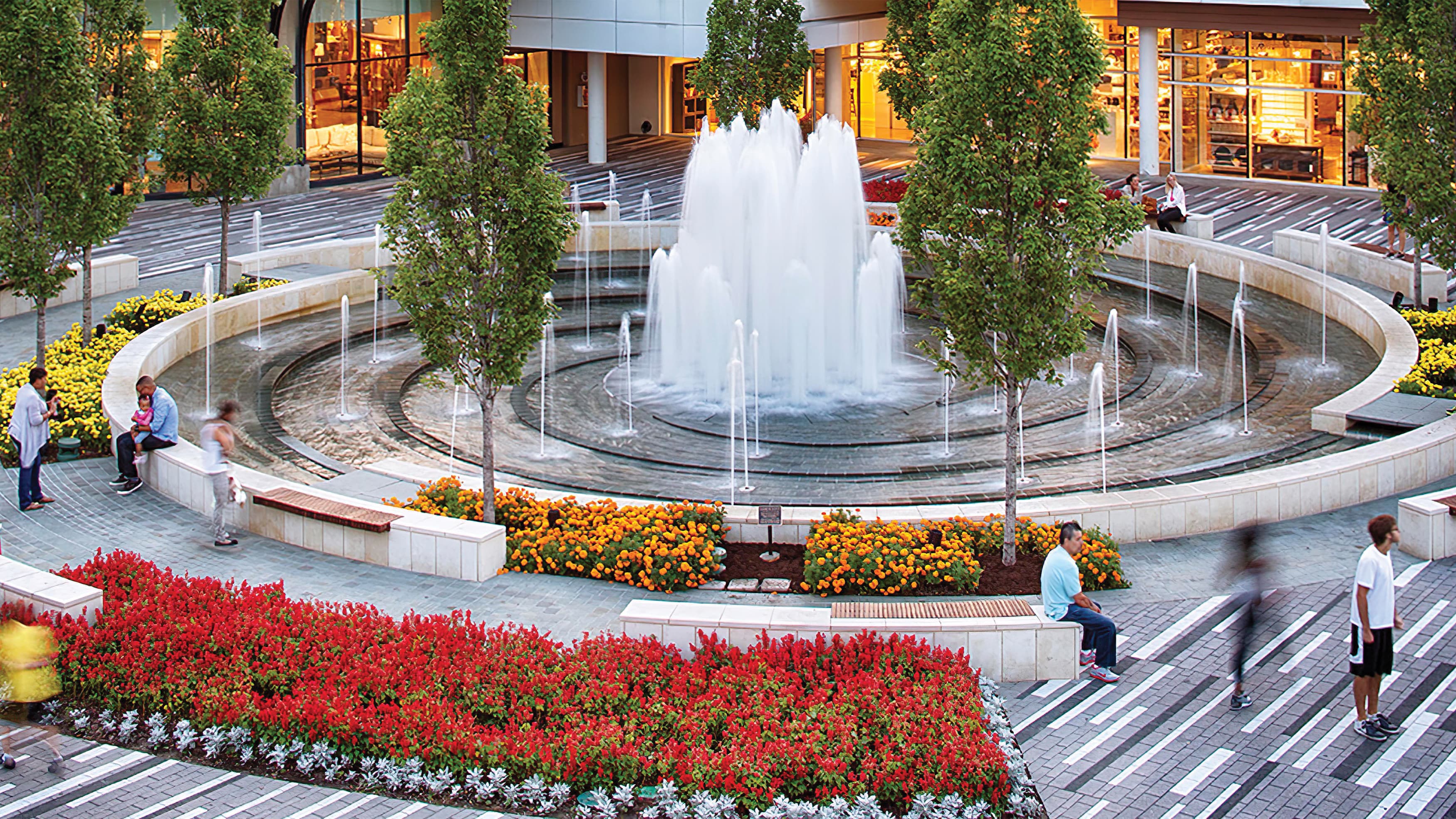 Fountain in center of plaza with surrounding seating and integrated flowered landscaping