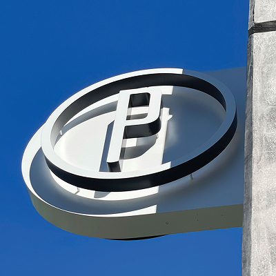Close-up of dimensional parking structure blade sign with custom monogram logo against blue sky at 845 San Carlos, exterior signage design by RSM Design